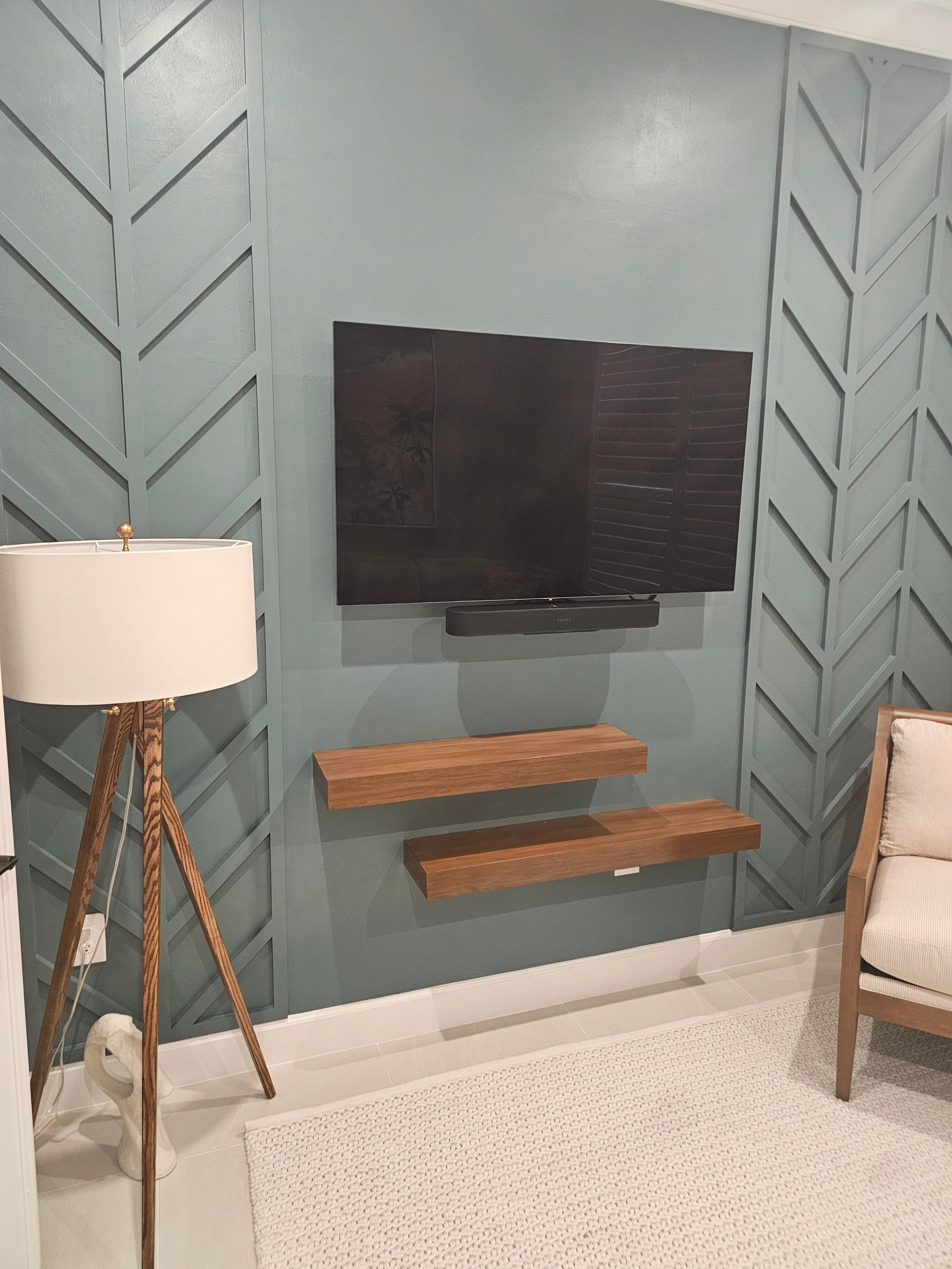Living room with mounted TV, wooden shelves, and a patterned accent wall.