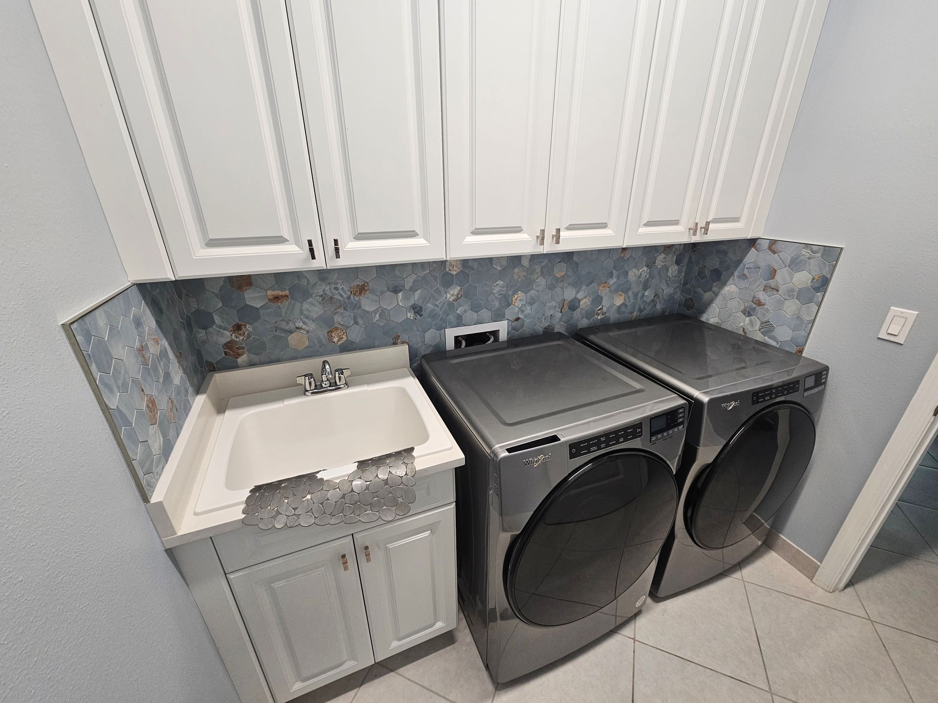 Laundry room with a washing machine, dryer, sink, and cabinets. Blue and white decor.