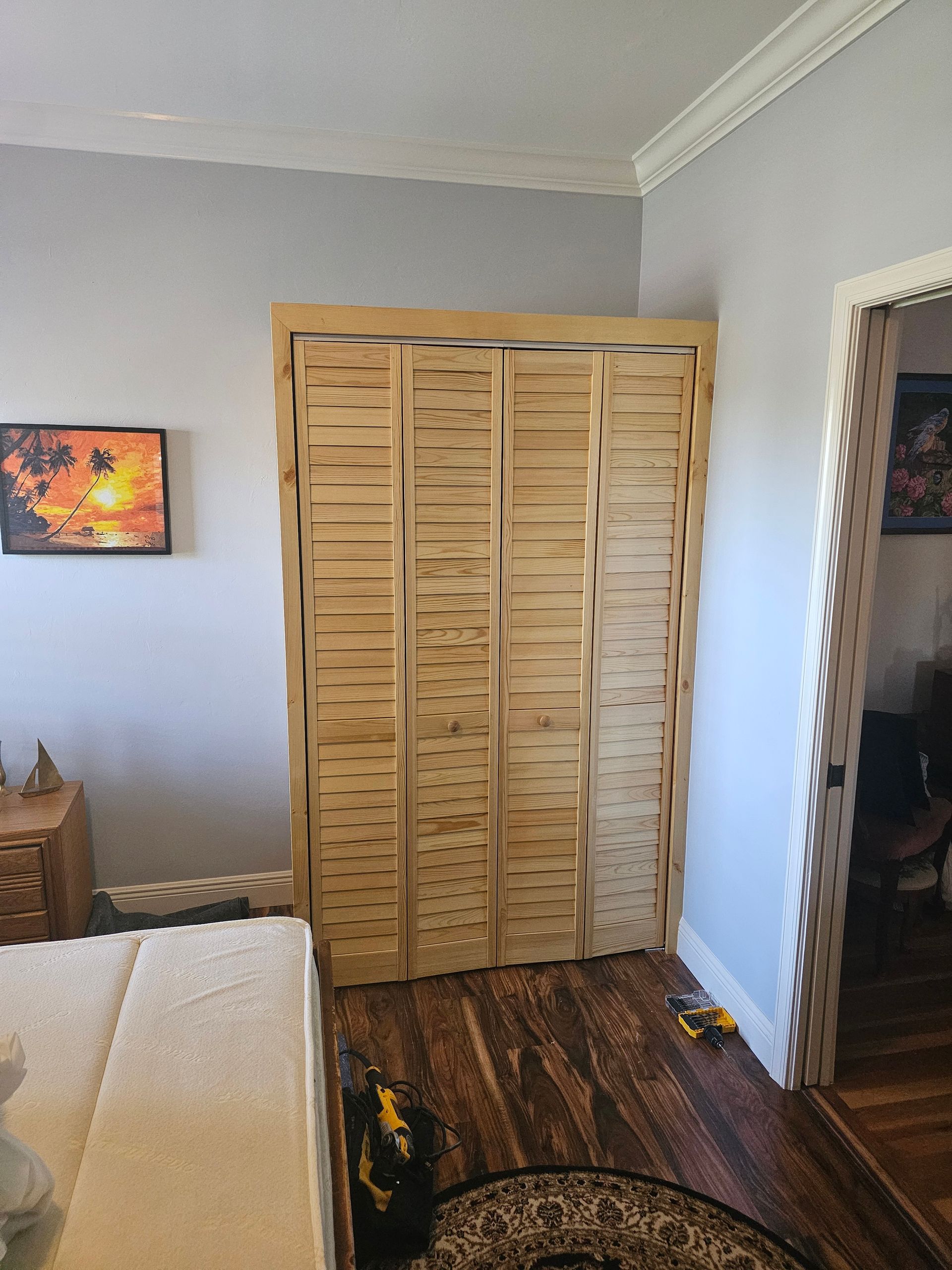 Wooden shutter doors in a room, next to a doorway, on a wood floor. A painting is visible.
