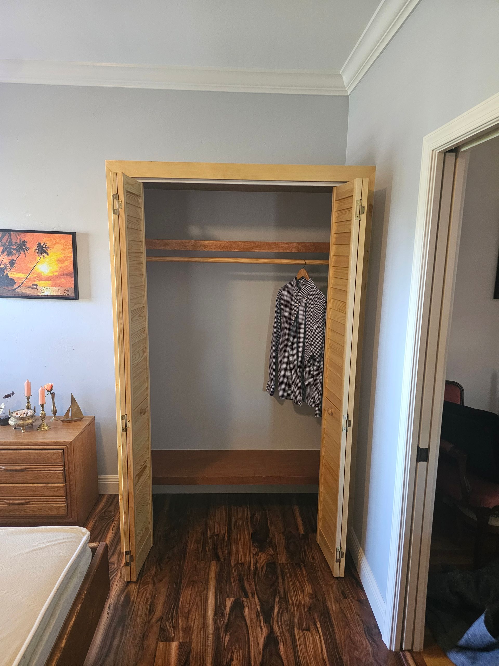 Wooden closet frame with clothes hanging inside, set in a room with hardwood floors and a door to the right.