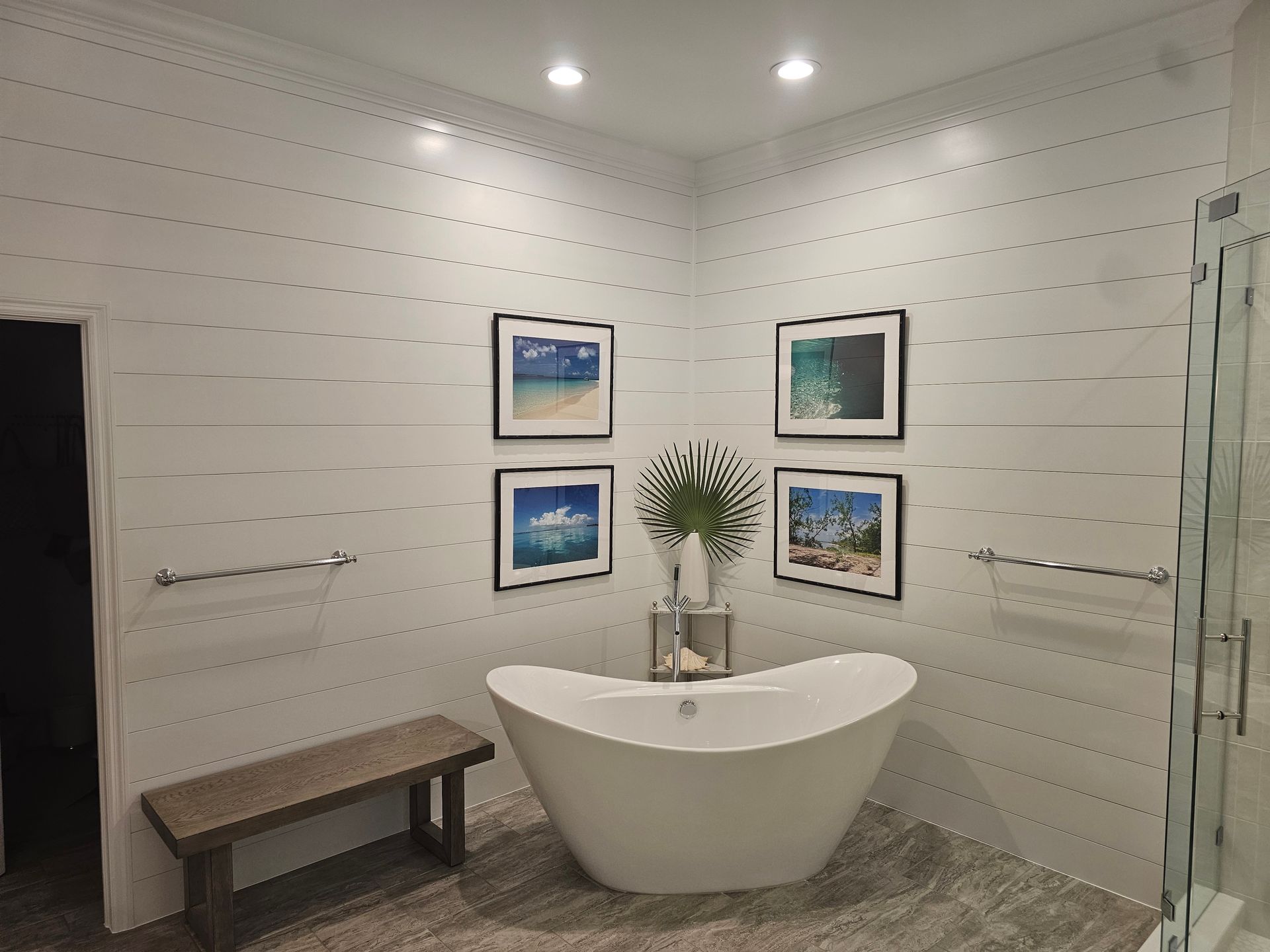 Modern bathroom with white shiplap walls, a freestanding tub, and framed art.