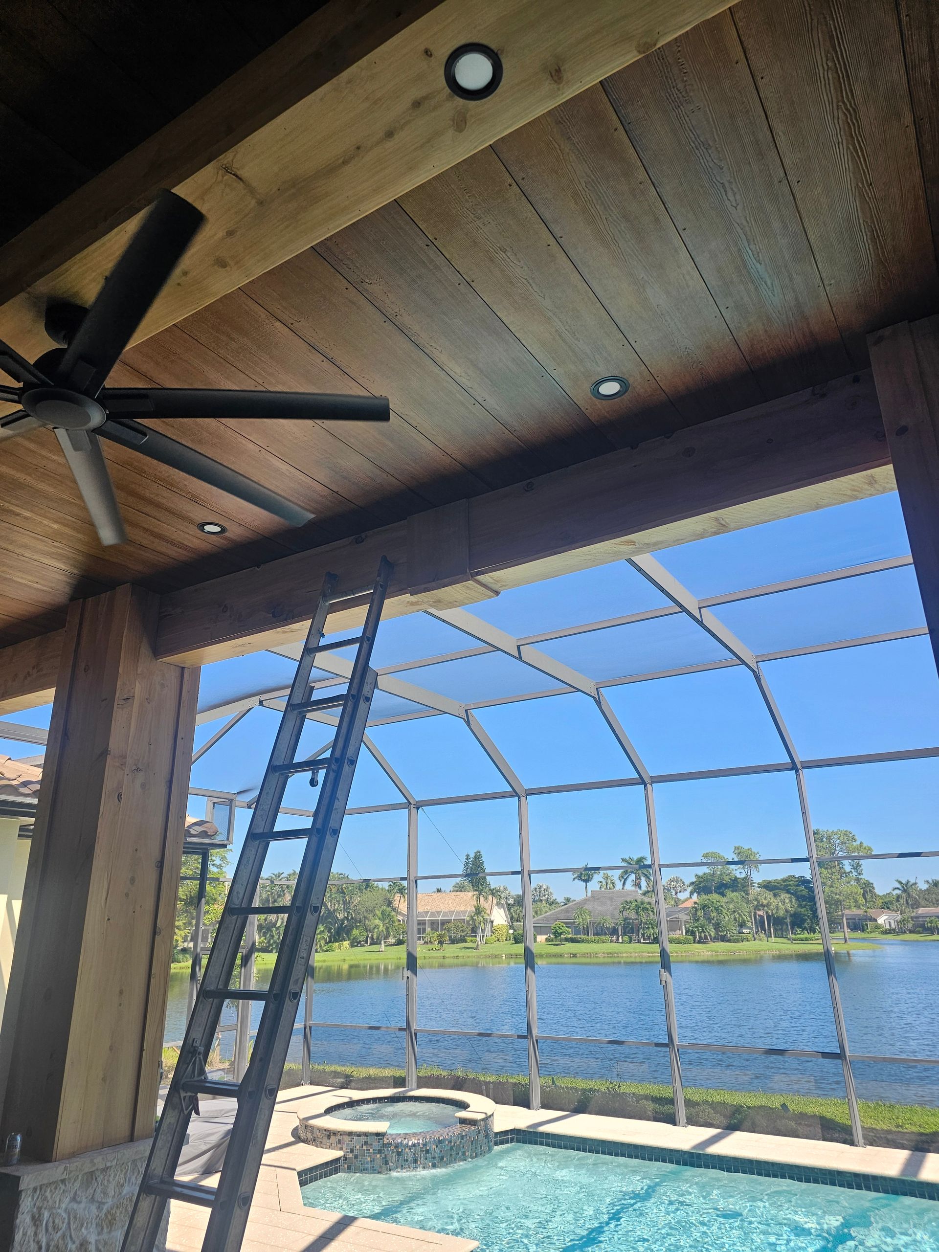 Patio with a pool and lake view; a ladder leans against the overhead structure.