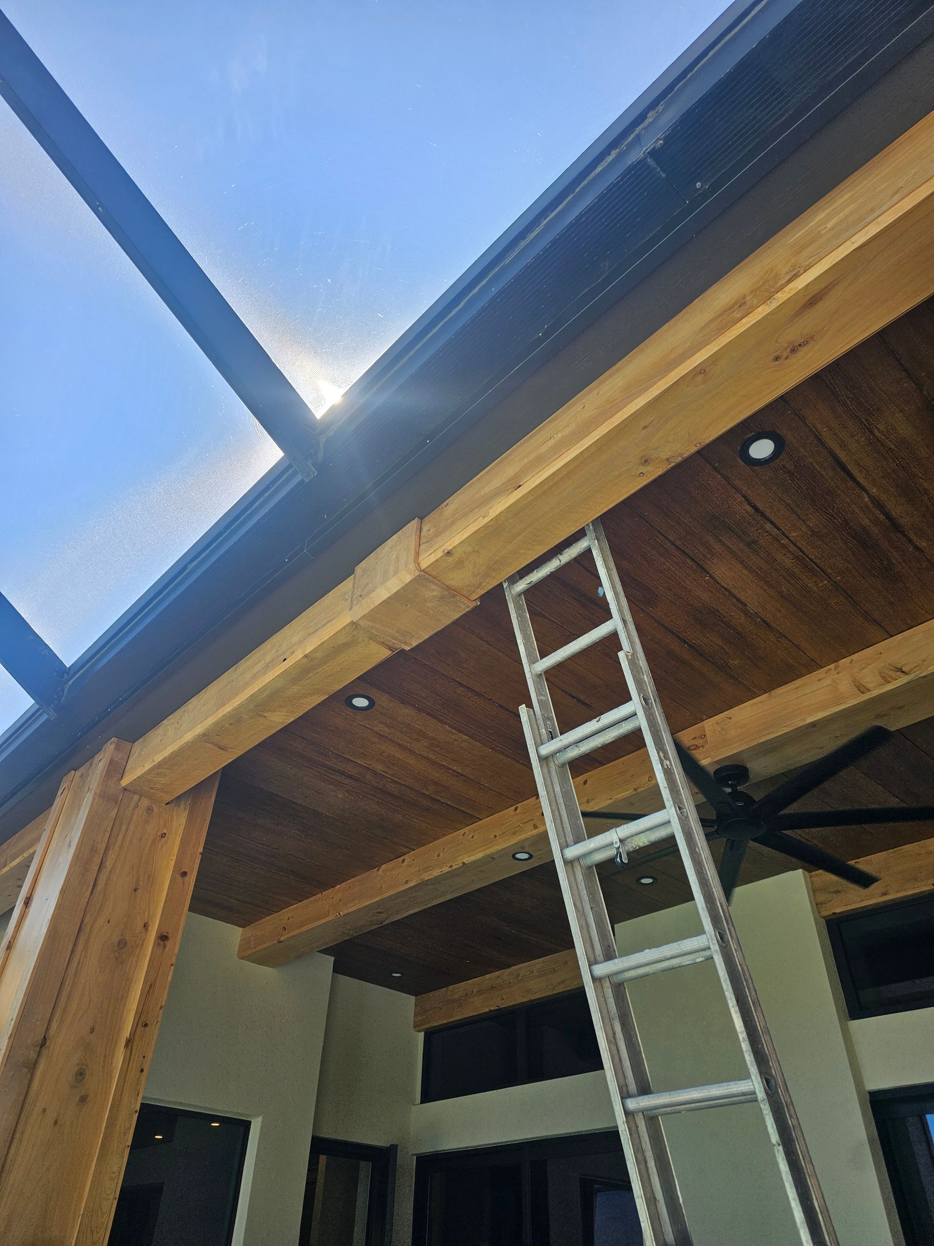 Ladder against a wood-beamed ceiling. Sun shines behind the structure.