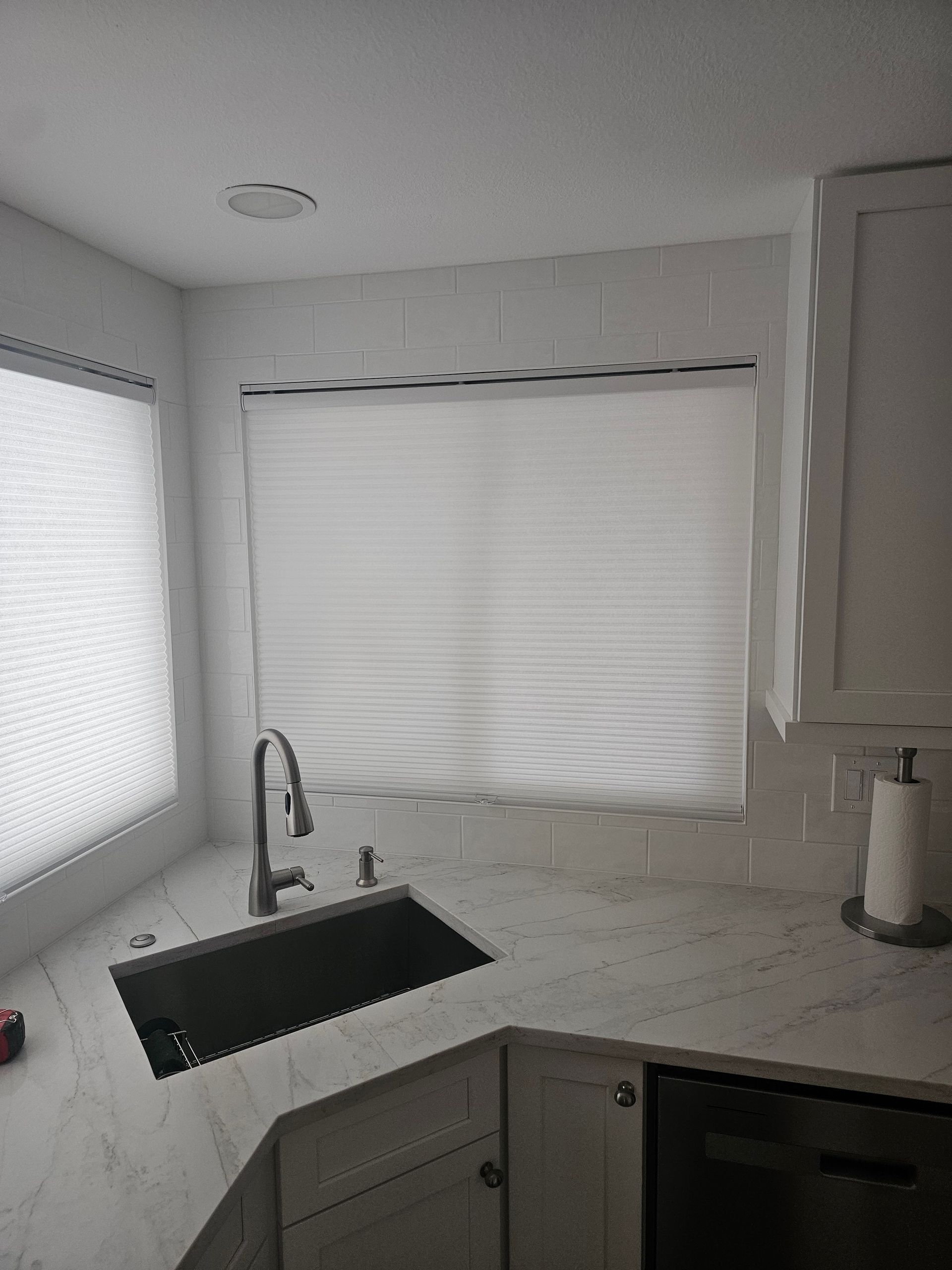 Kitchen corner with a sink, faucet, white countertop, and window with closed blinds.