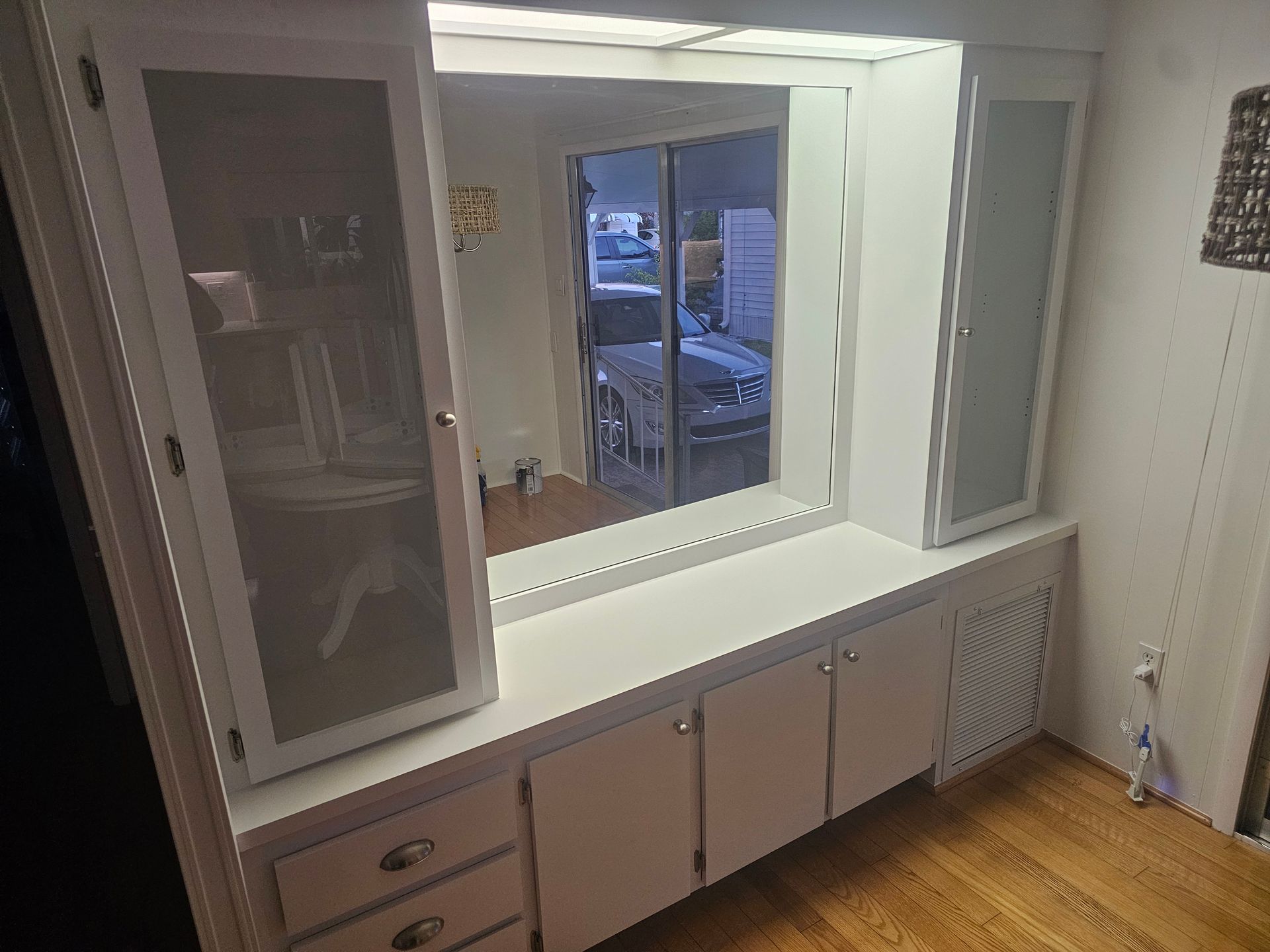 White built-in storage unit with a mirror, cabinets, and drawers in a room with wood flooring.