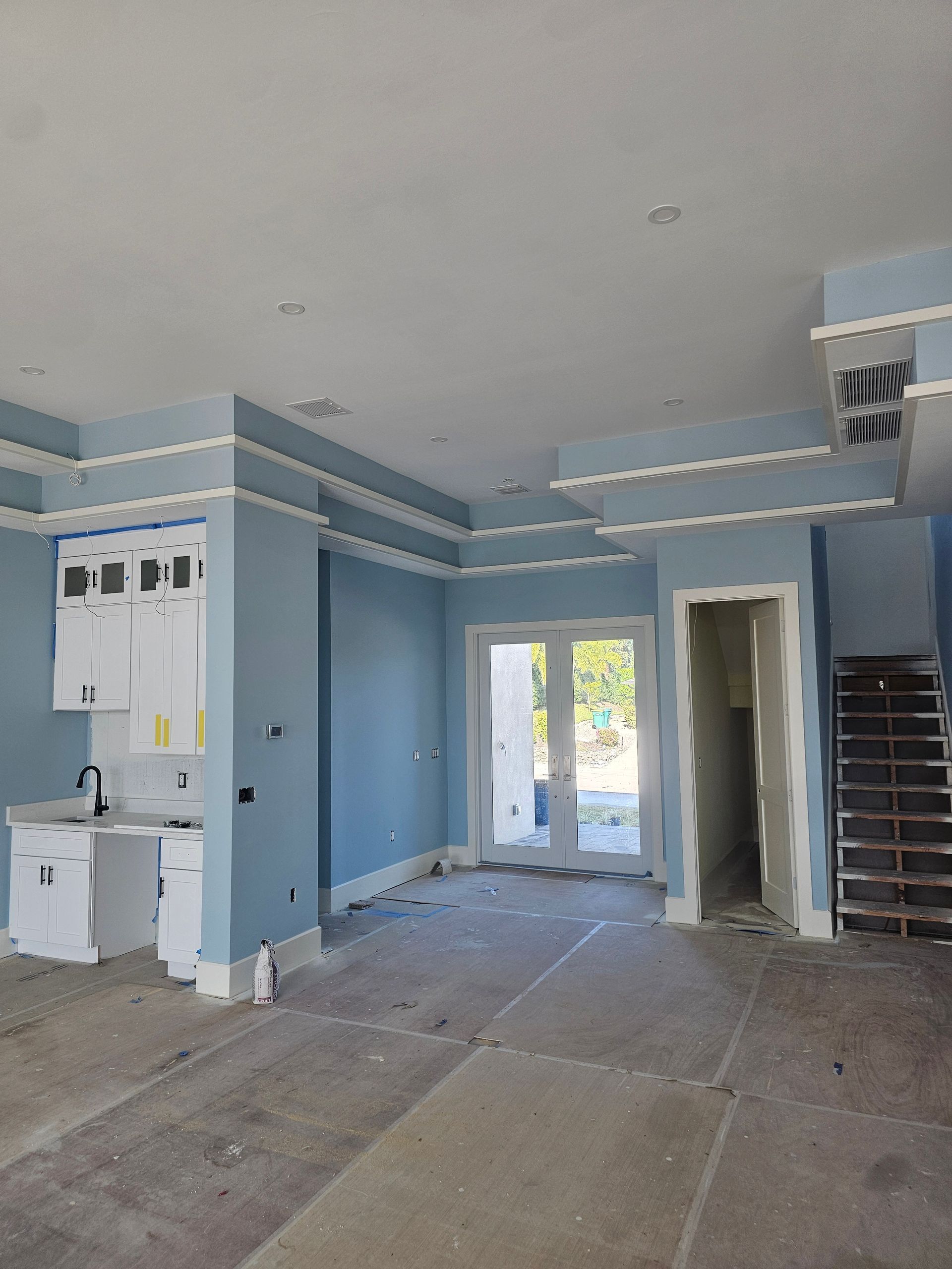 Interior room under construction, light blue walls, white trim, cabinets, doorway, stairs, and concrete floor.