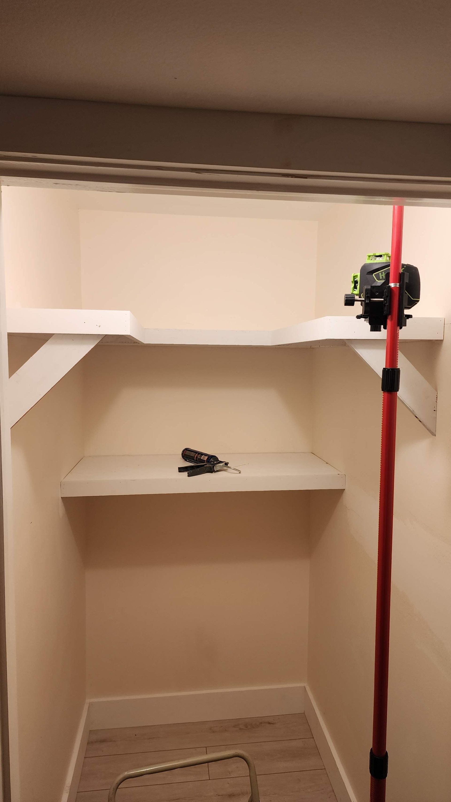 Closet with two shelves, white walls, and a laser level on a red pole.