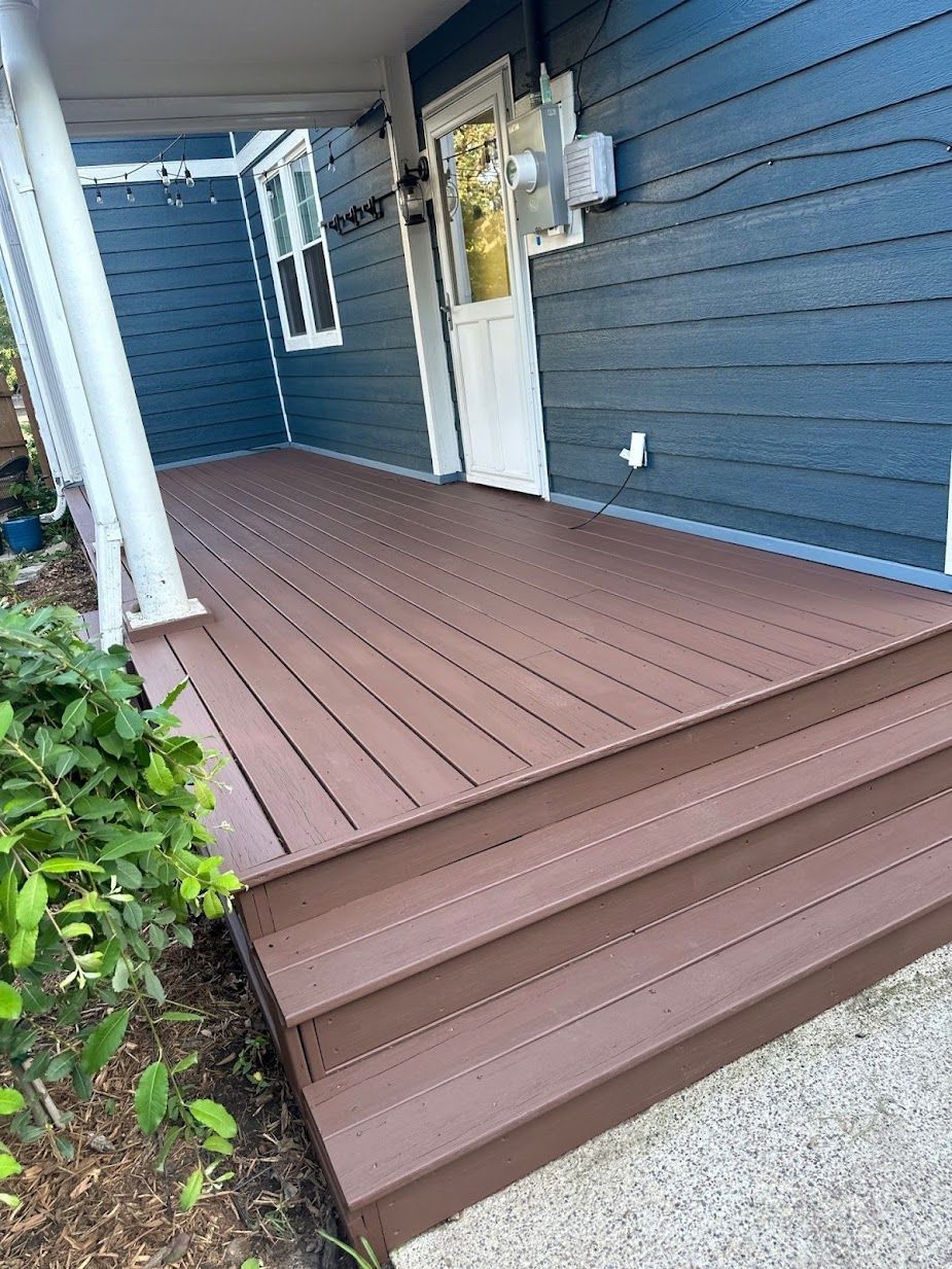 A blue house with a brown deck and stairs in front of it.