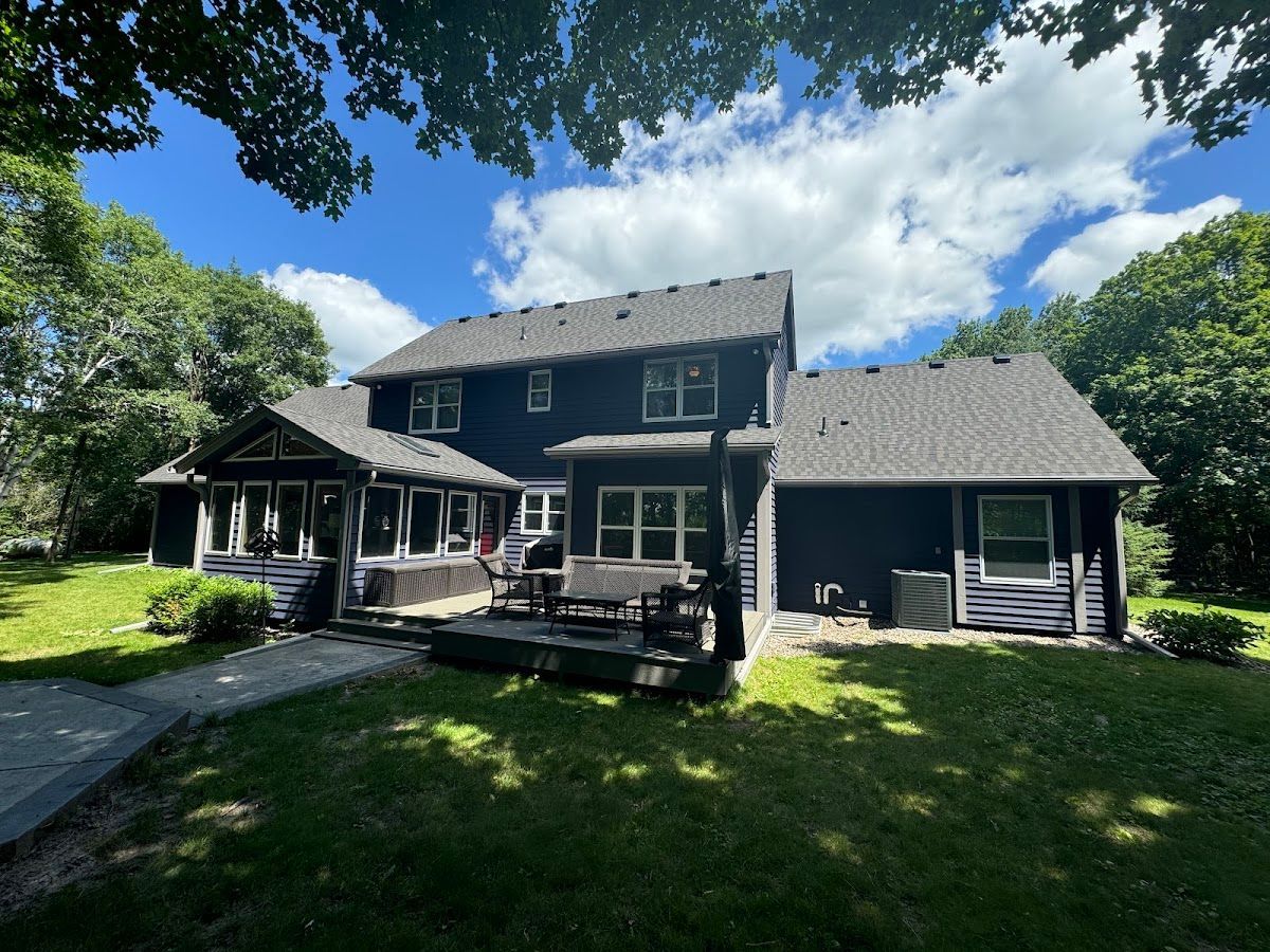 A large black house with a gray roof is surrounded by trees and grass.