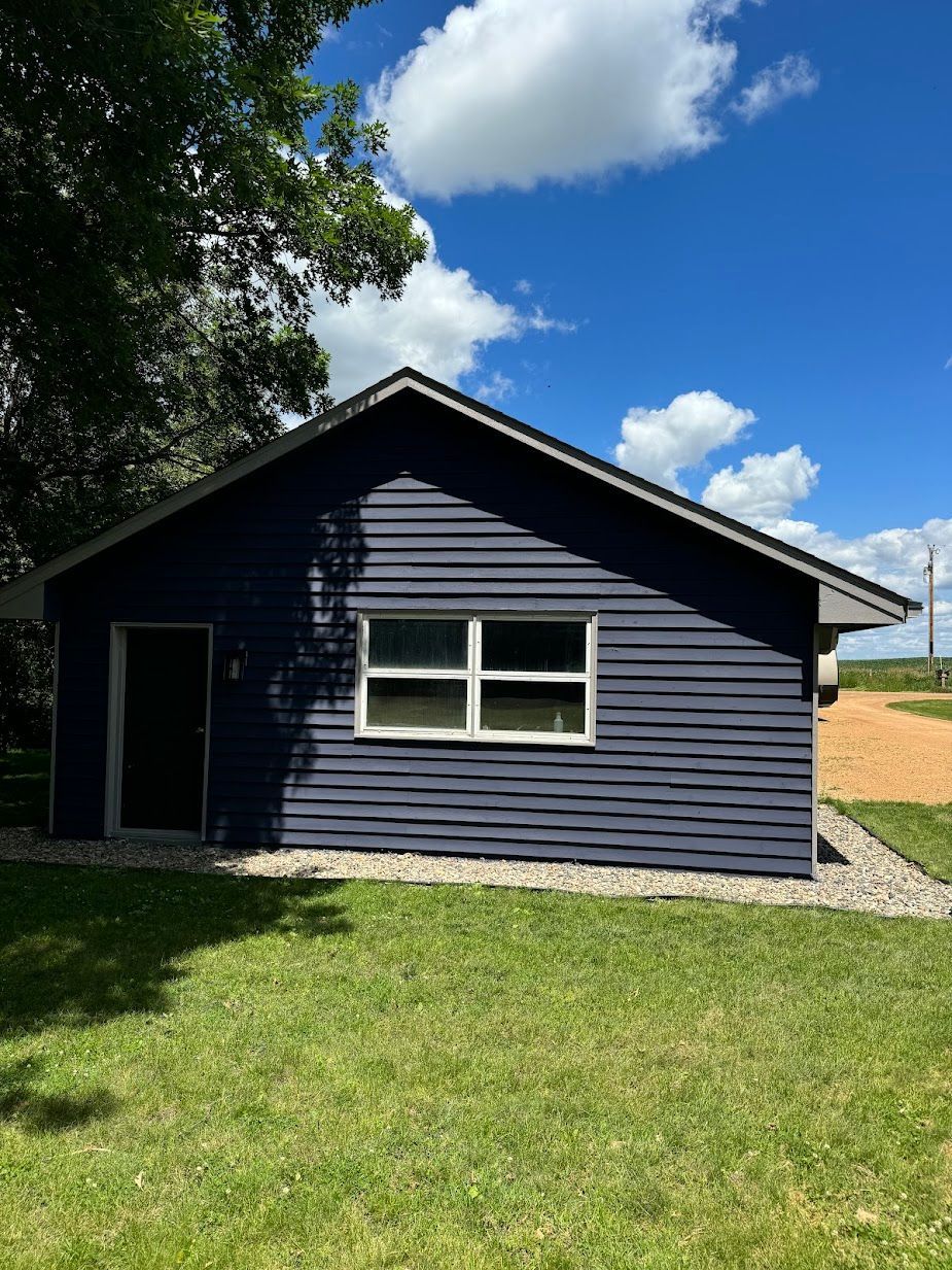 A small blue house with a white window is sitting in the middle of a lush green field.