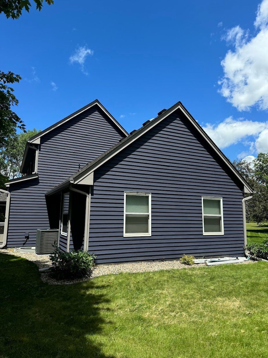 A house with a blue siding and white windows is sitting on top of a lush green field.
