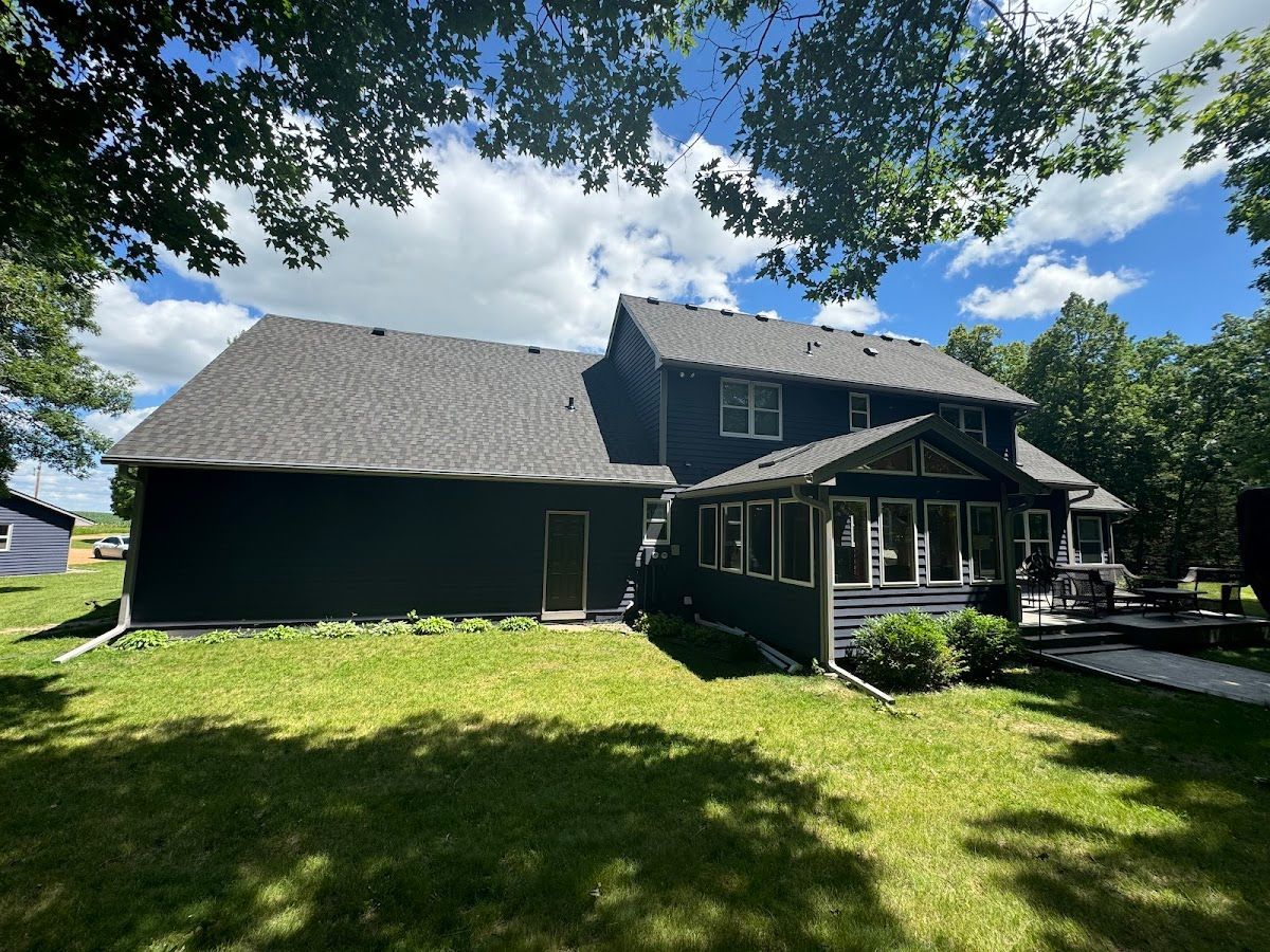 A large black house with a black roof is sitting on top of a lush green field.