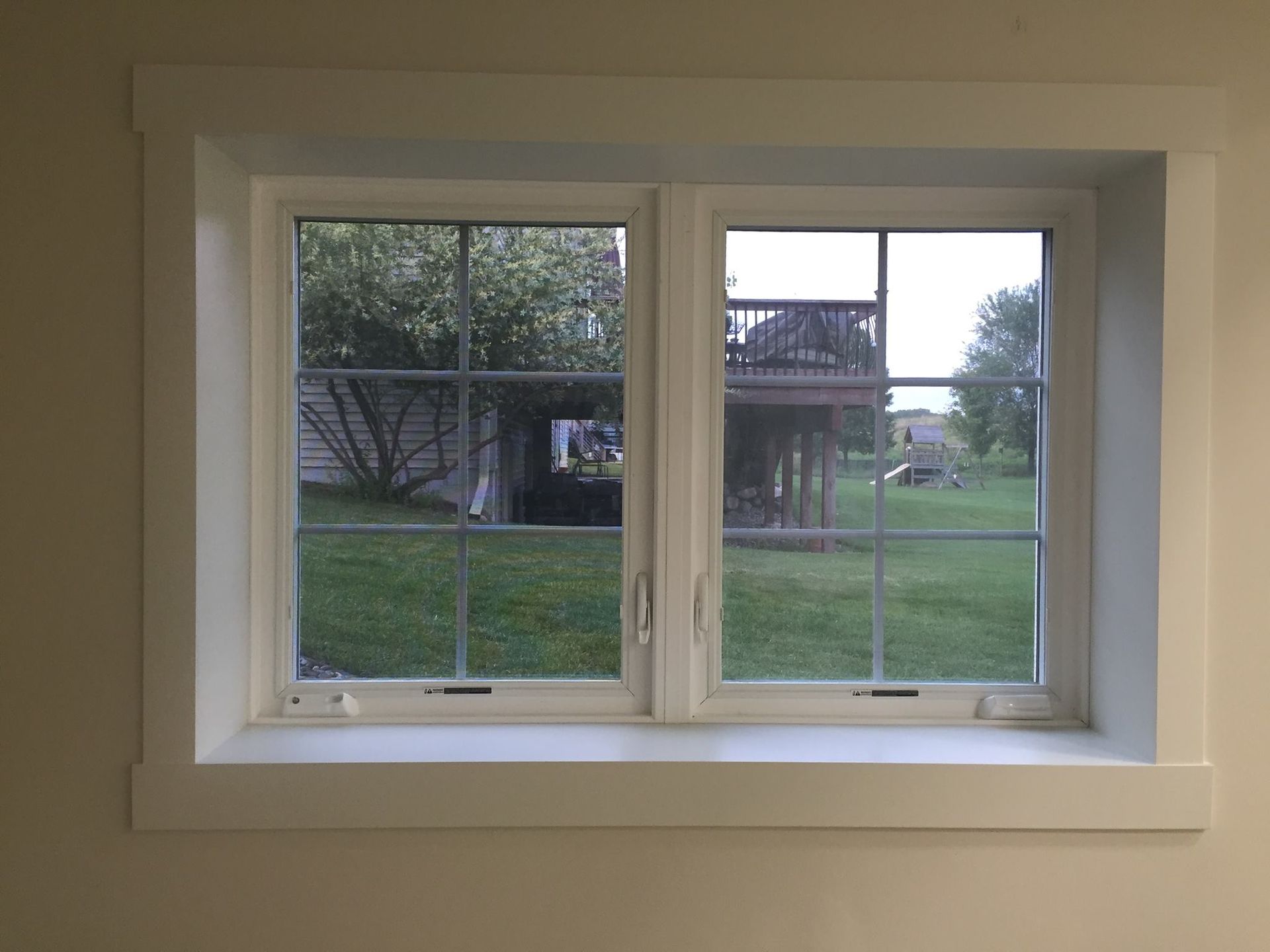 A white window with a view of a yard and a deck.