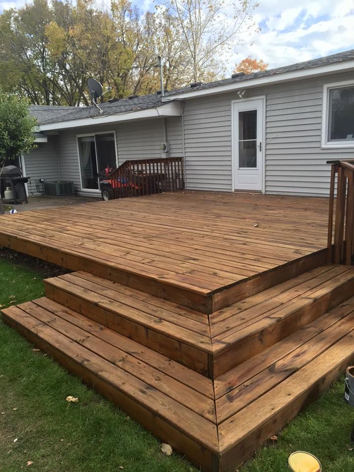 A large wooden deck with stairs is in front of a house.