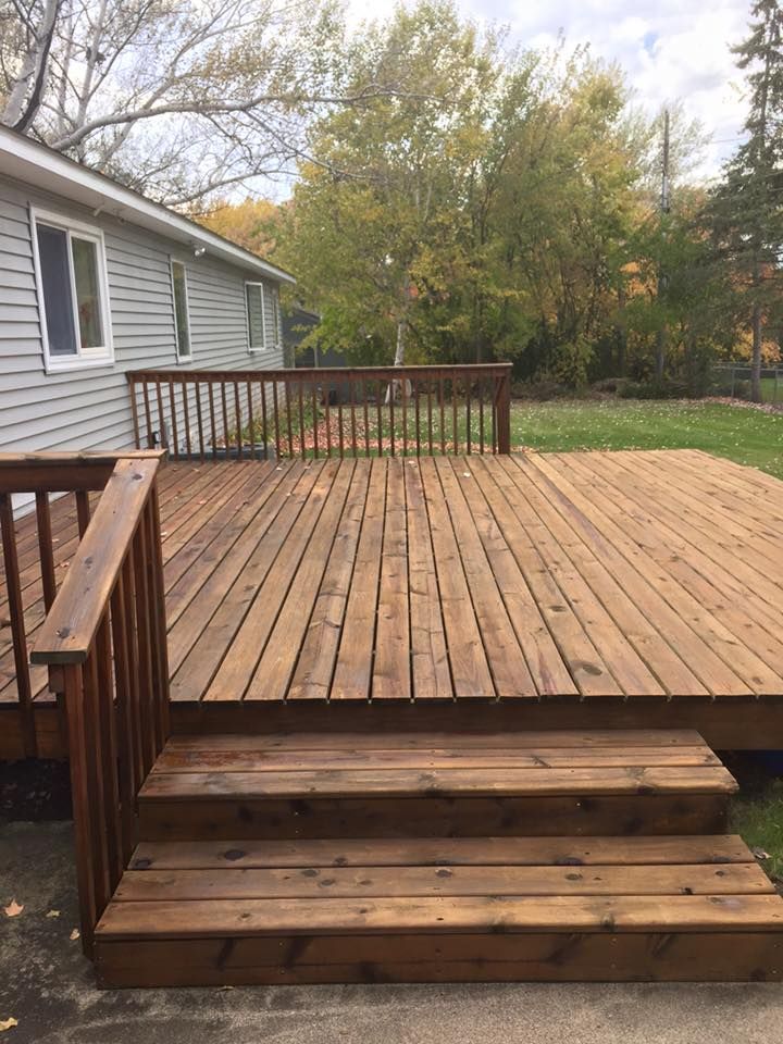 A large wooden deck with stairs leading up to it is in front of a house.