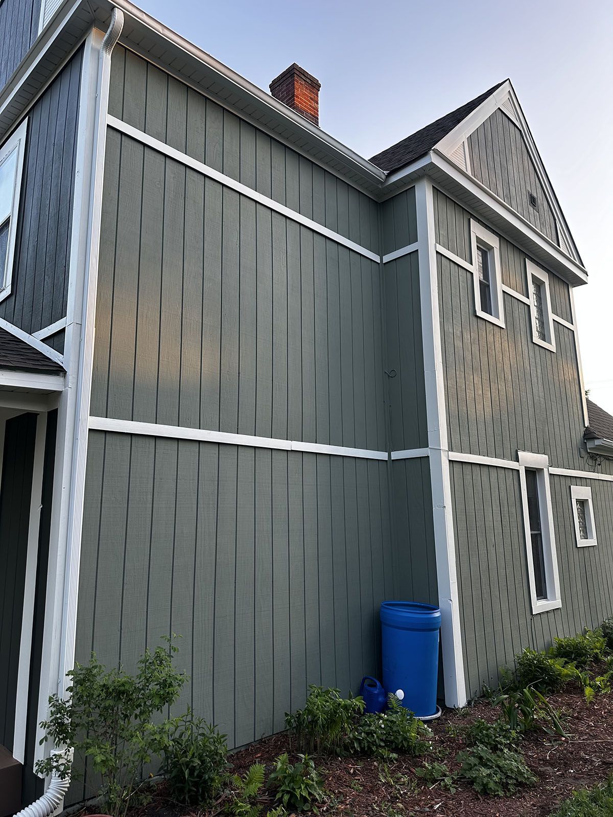 A large house with a blue trash can in front of it.