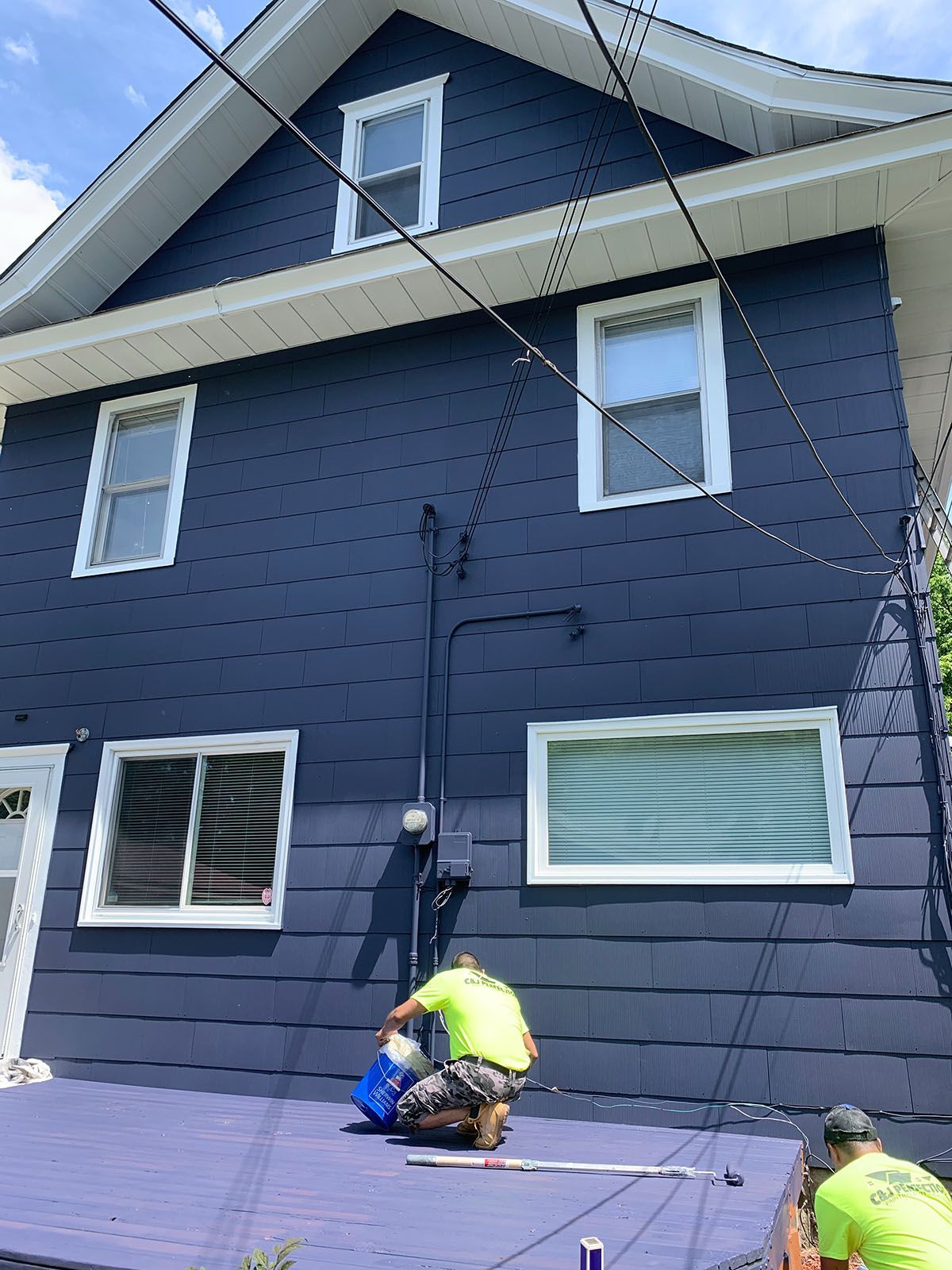 Two men are painting the side of a blue house.
