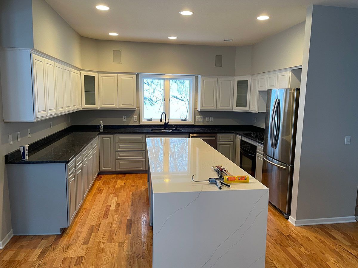 A kitchen with white cabinets , black counter tops , stainless steel appliances and a large island.