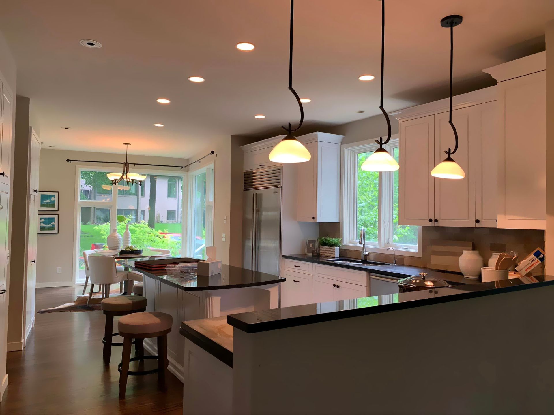 A kitchen with white cabinets and stools and a dining room in the background