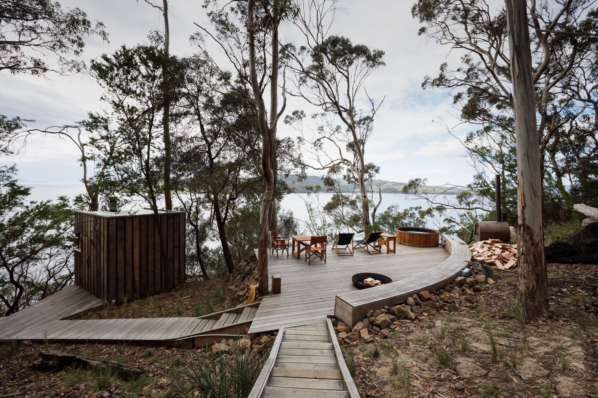 A wooden walkway leading to a patio overlooking a body of water surrounded by trees.