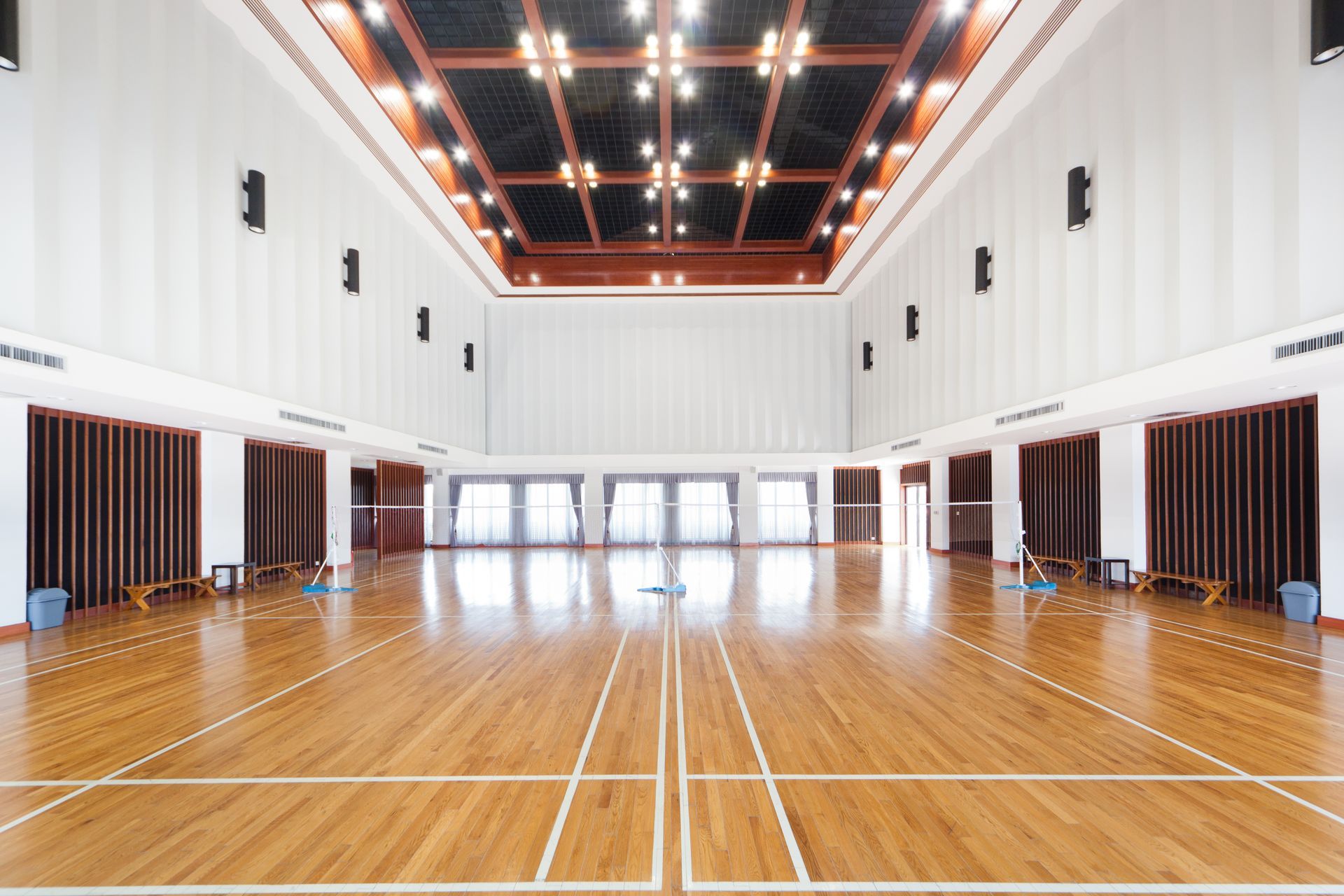 Empty indoor gymnasium with polished wooden floor, white walls, and bright ceiling lights Empty indoor gymnasium with polished wooden floor, white walls, and bright ceiling lights