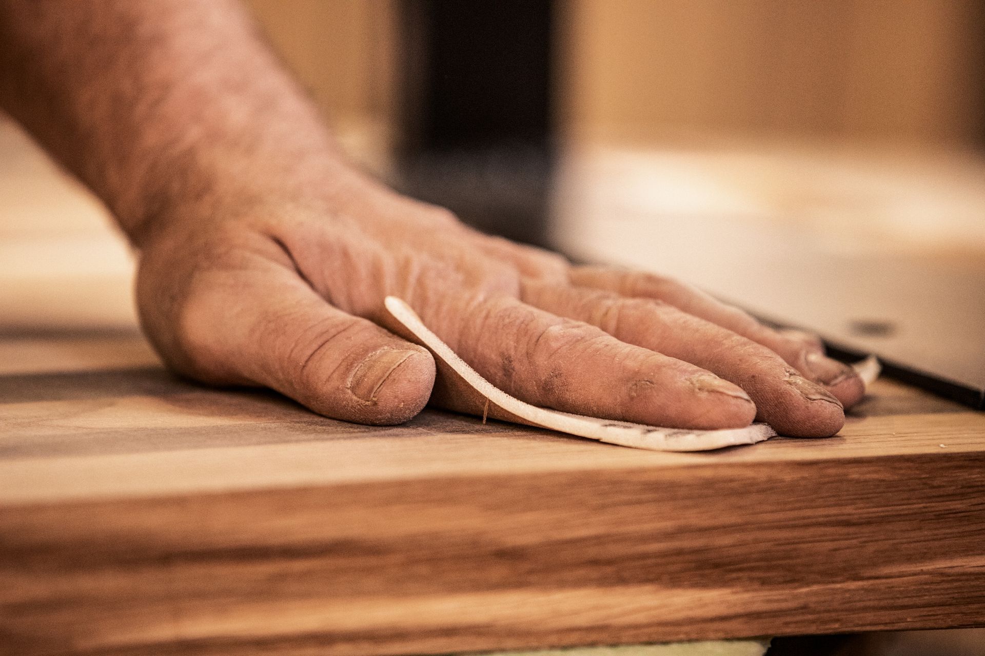 A mature carpenter smoothing a Tasmanian Oak plank with sandpaper during custom joinery work. A mature carpenter smoothing a Tasmanian Oak plank with sandpaper during custom joinery work.