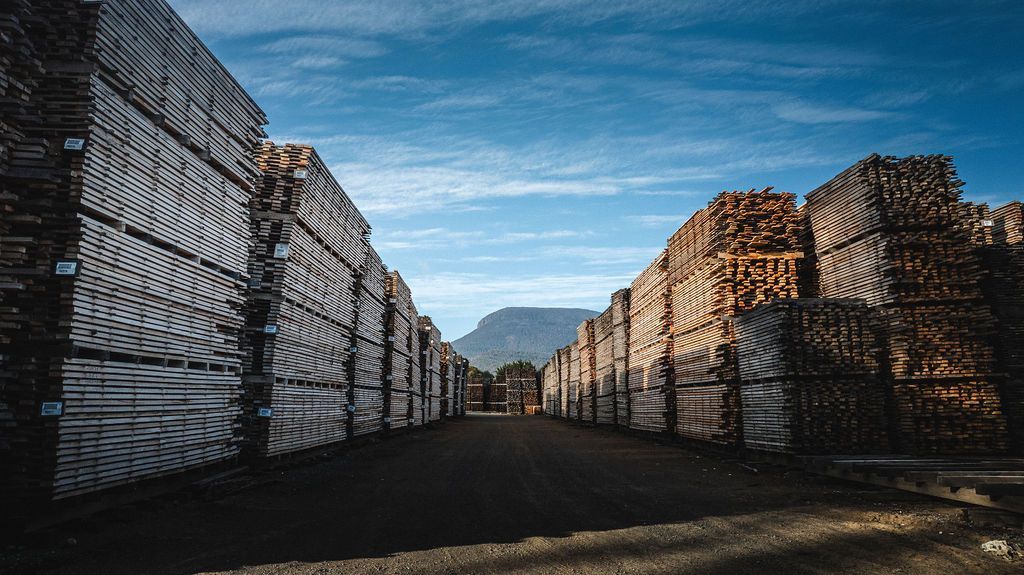 A flatbed truck parked on a gravel lot near industrial buildings under a cloudy sky.