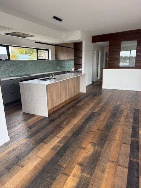 Modern open-plan kitchen and living area featuring Tasmanian Oak flooring, a sleek island bench, and contemporary cabinetry.