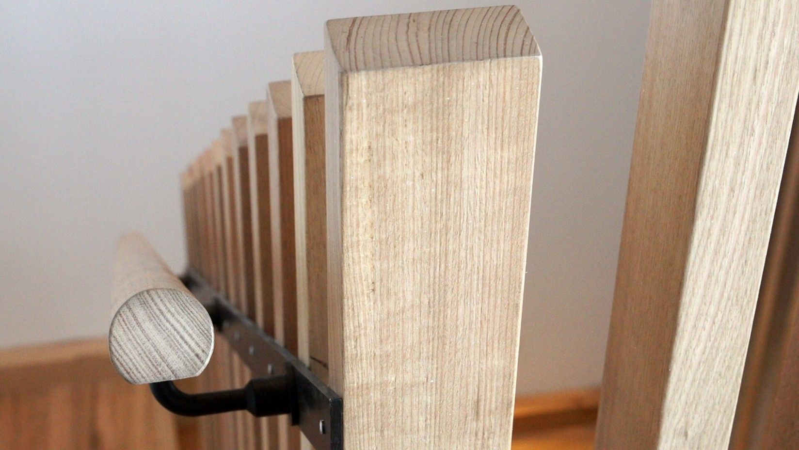 Close-up of a timber balustrade showing vertical hardwood slats, a rounded timber handrail, and natural wood grain finish.