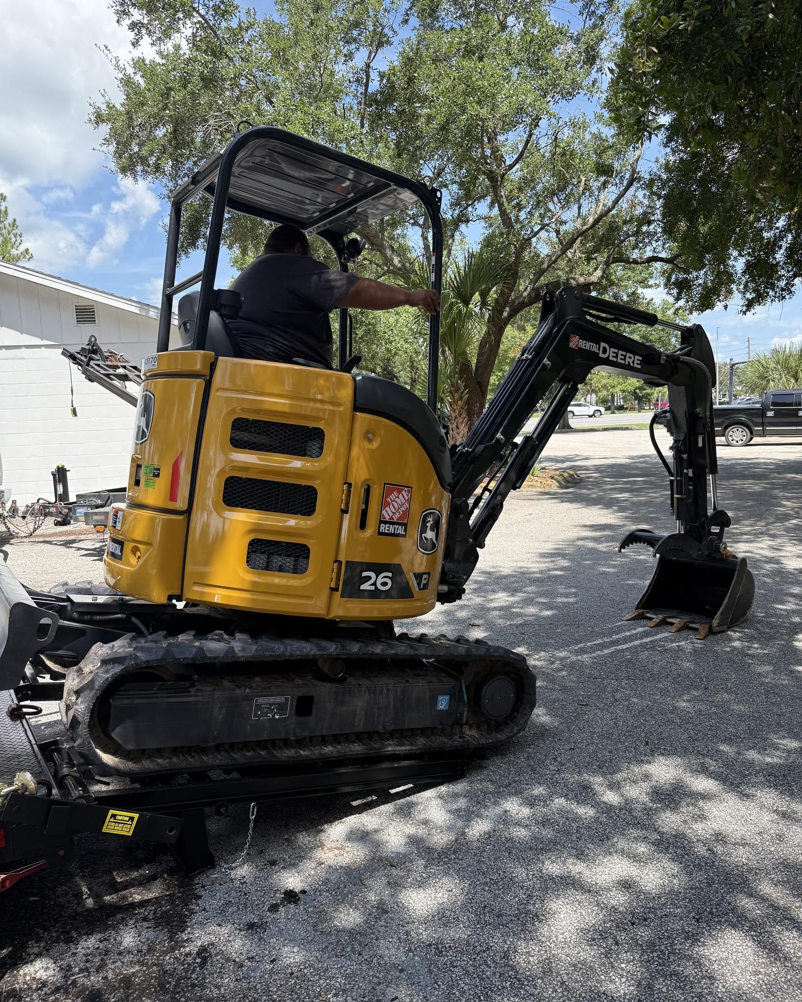 A yellow mini excavator with a person inside, operating it outdoors on gravel.