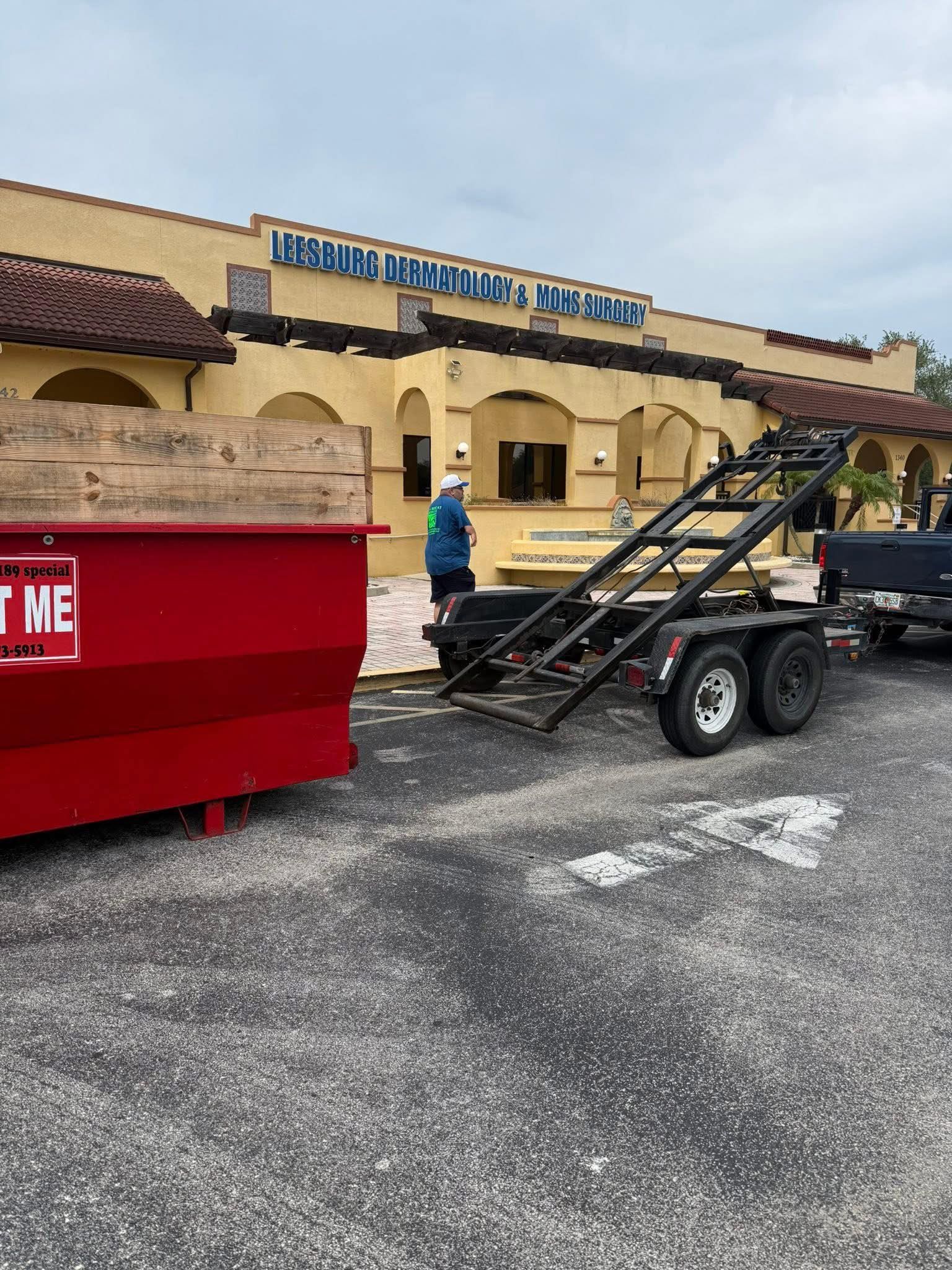 Red dumpster and trailer next to restaurant, person loading debris.
