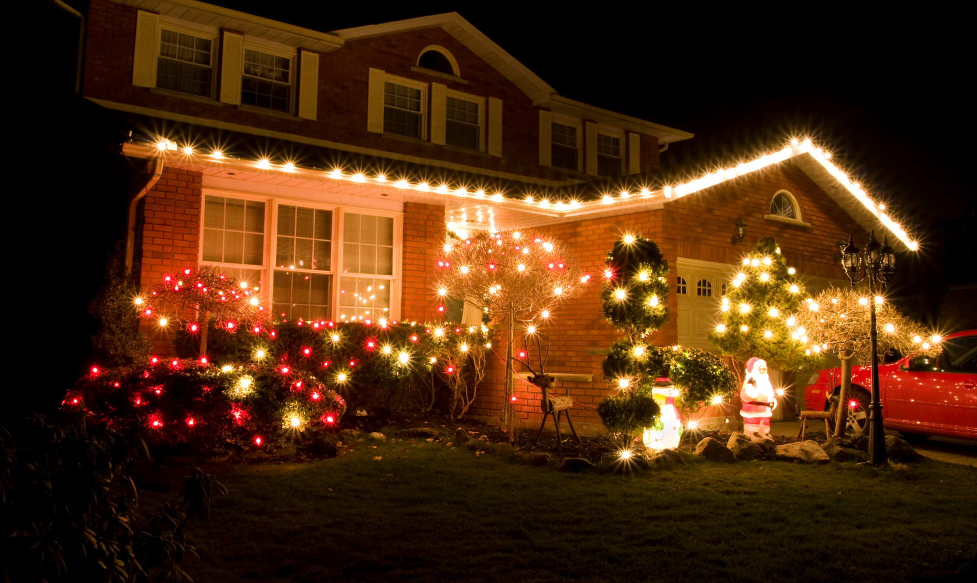 A house at night is decorated with Christmas lights in red and yellow, with a Santa decoration in the yard.