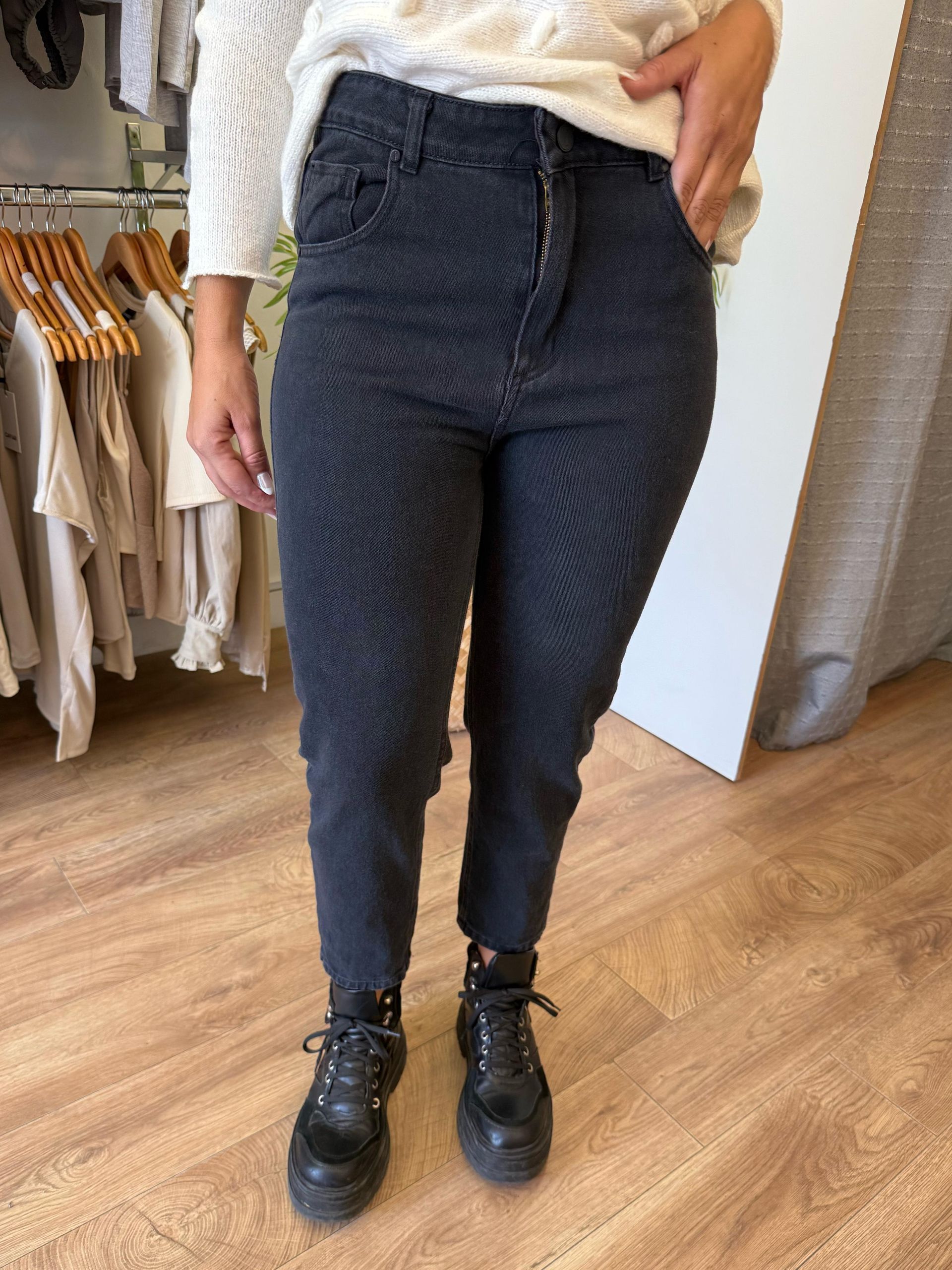 Una mujer que viste un suéter blanco y jeans negros está parada sobre un piso de madera.