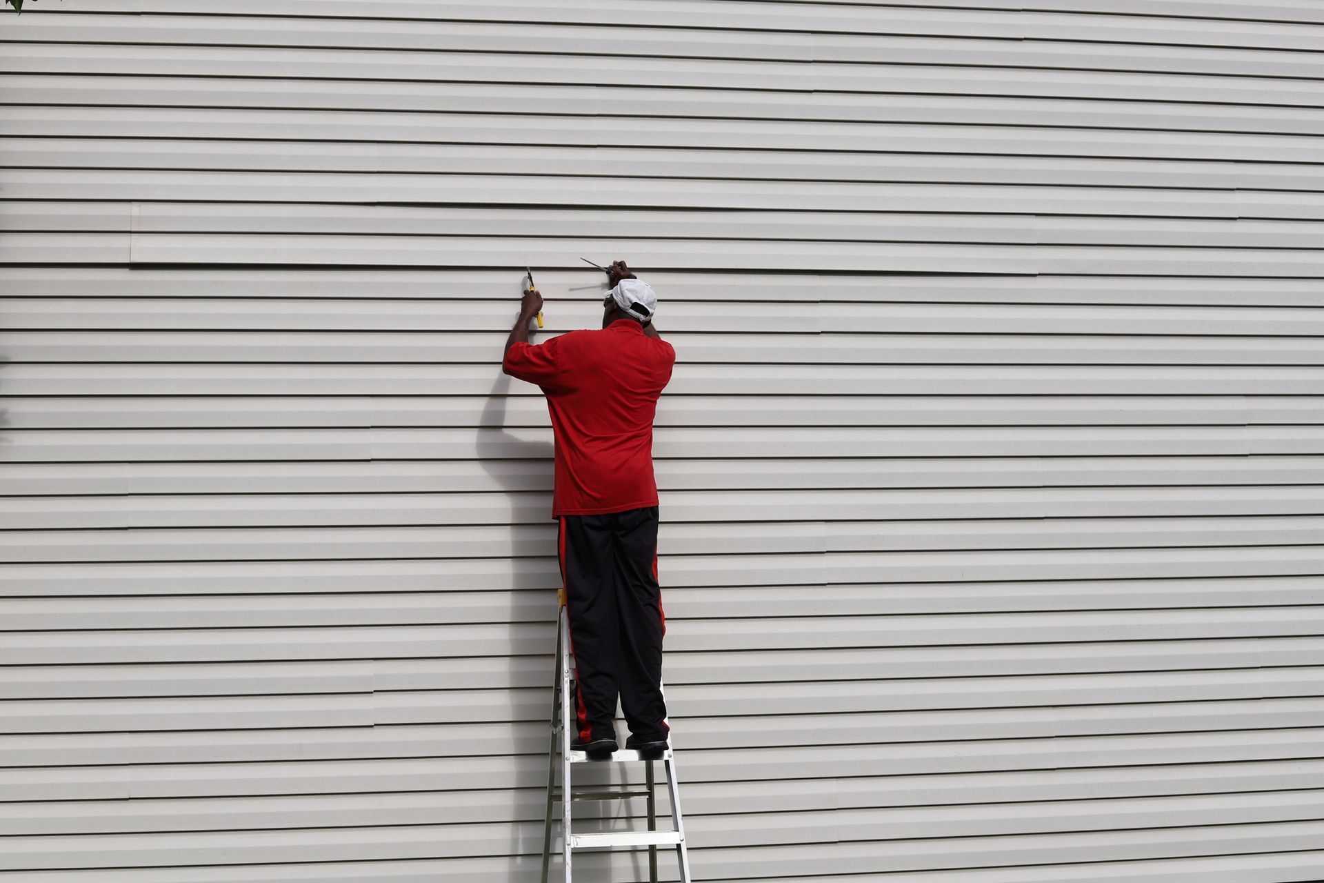 A man is standing on a ladder next to a white wall.