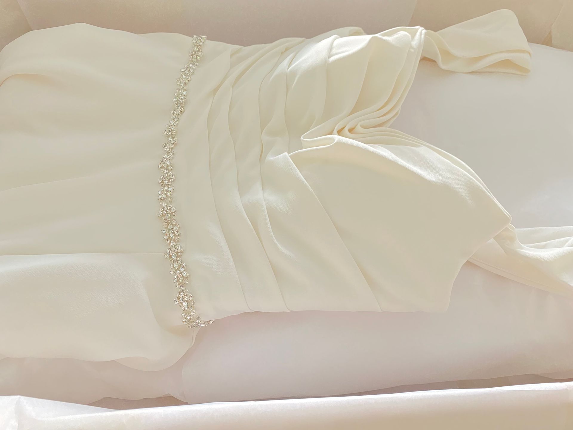 Cream-colored wedding dress with beaded belt, neatly folded in a white box.