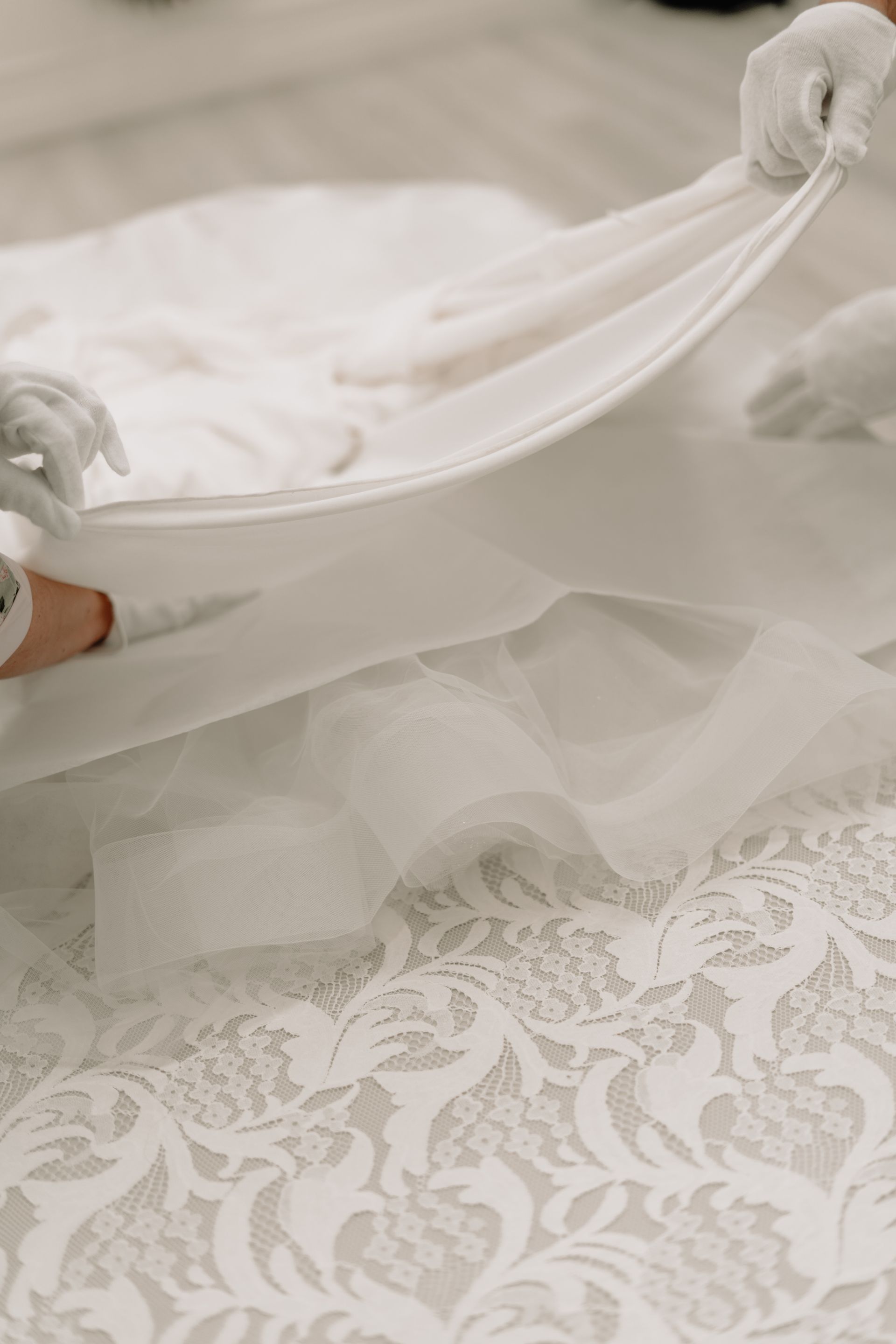 Hands in white gloves carefully unfolding a white lace bridal gown.