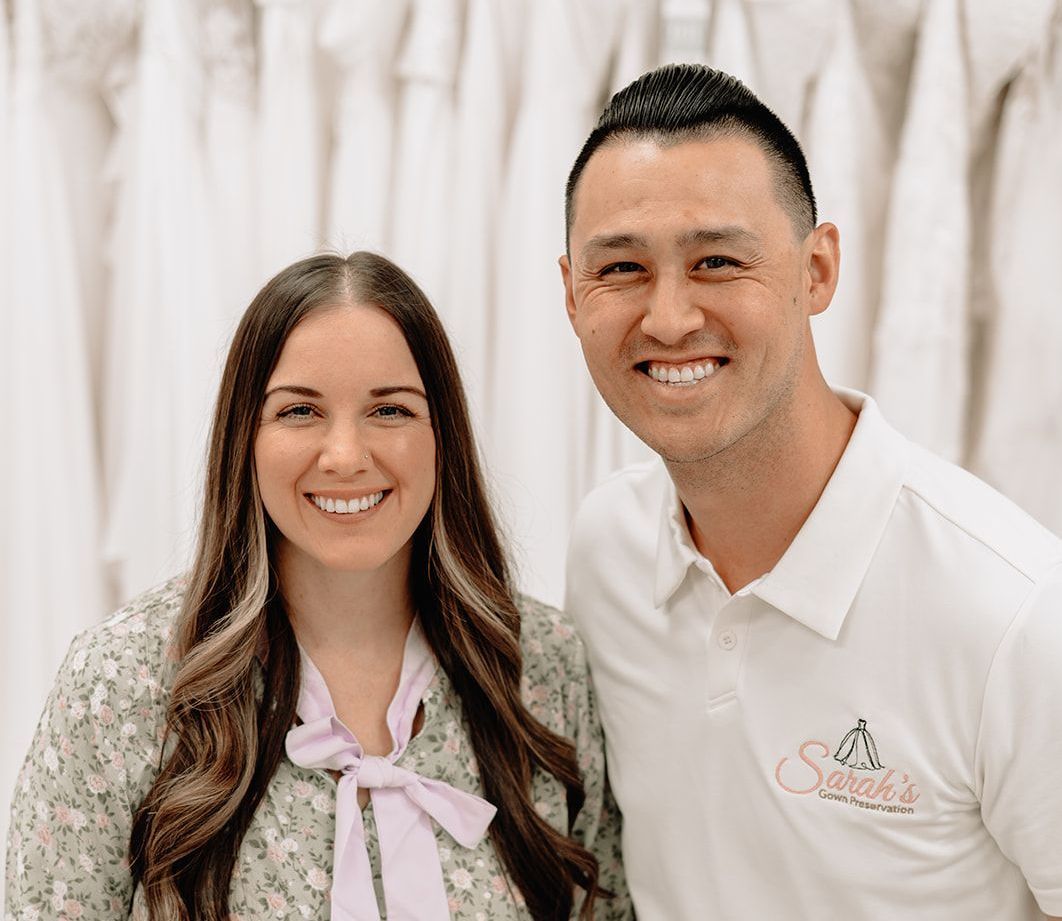 Woman and man smiling at the camera in a bridal shop. Dresses are visible in the background.