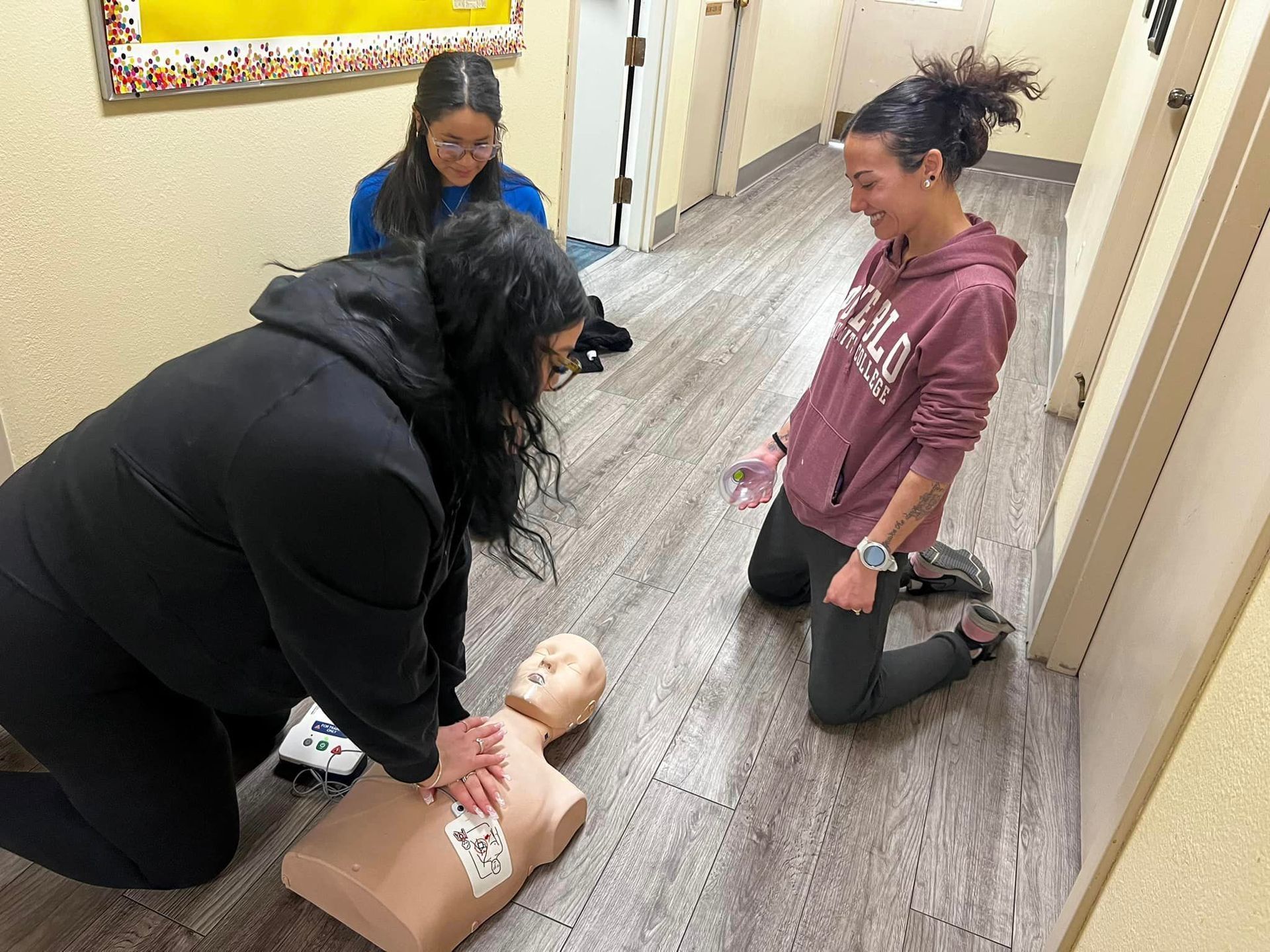 A woman is kneeling down next to a mannequin in a hallway.