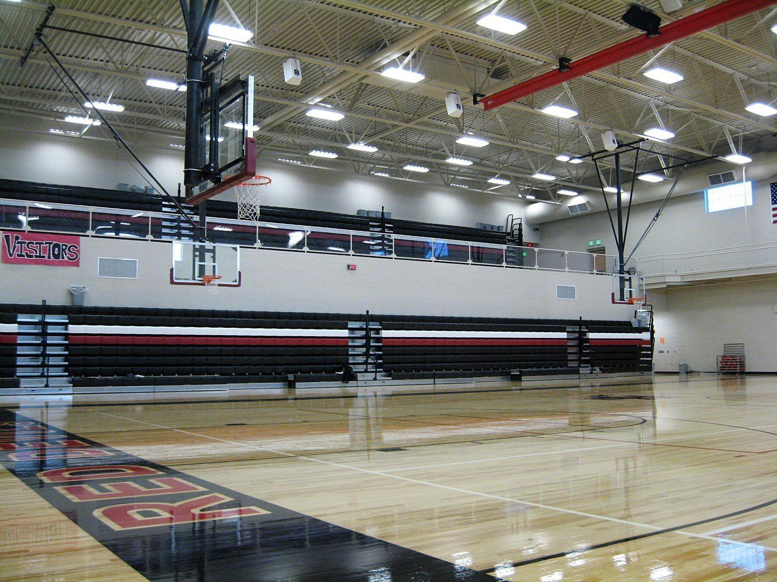 Empty indoor basketball court with polished wooden floors and retractable bleachers.