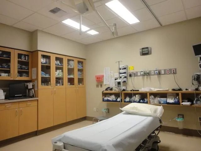 A clean, organized hospital room with a neatly made patient bed in the foreground.