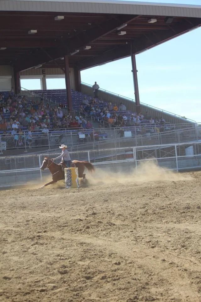 Cowgirl on a horse makes a sharp turn kicking up dust beside a barrel in a rodeo arena. 