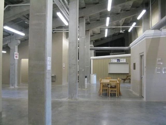 Industrial meeting space with concrete pillars, metal ducts, fluorescent lights, and wooden tables.