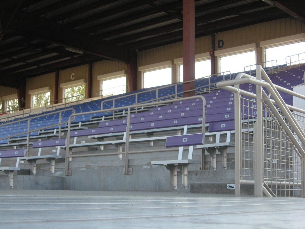 Empty stadium seats with purple and blue colors under a metal roof. 