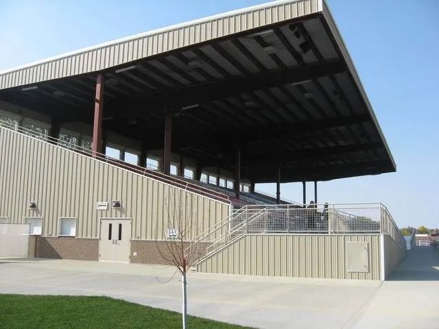 A large covered metal stadium or grandstand with tiered seating, open sides, and a concrete exterior. 