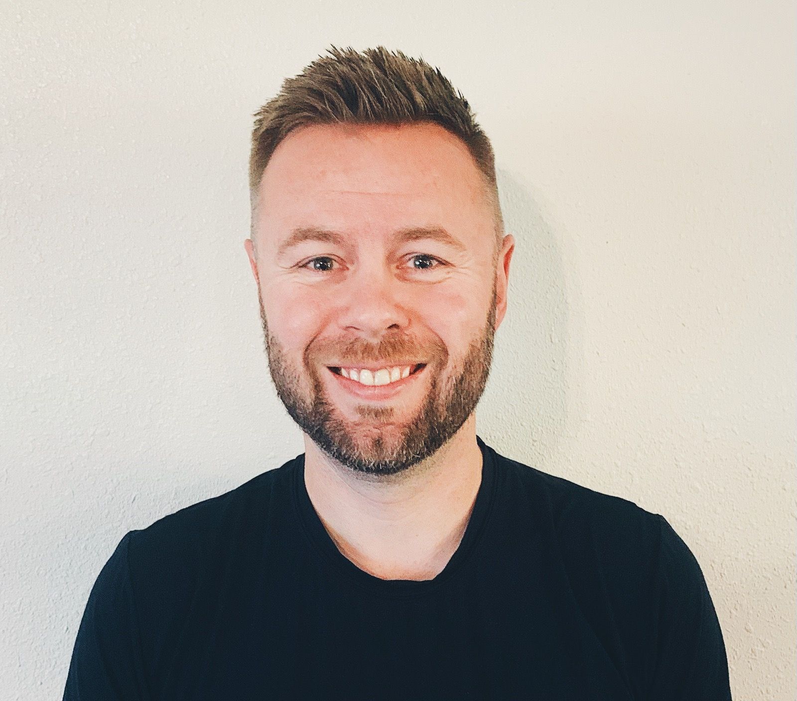 A man with a beard is smiling for the camera while wearing a black shirt.