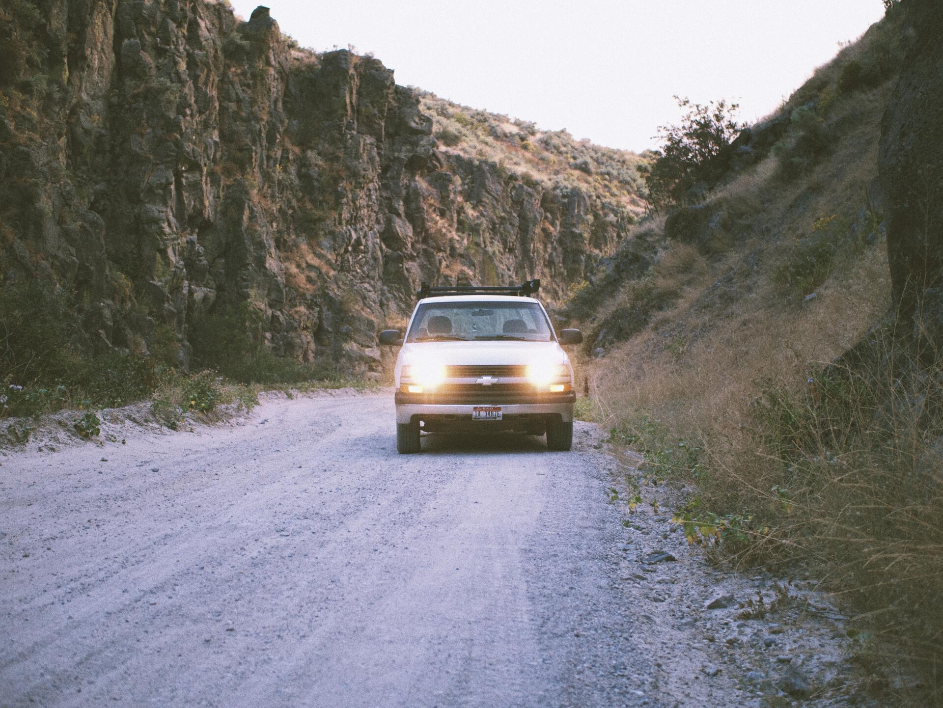 A car is driving down a dirt road in the mountains.