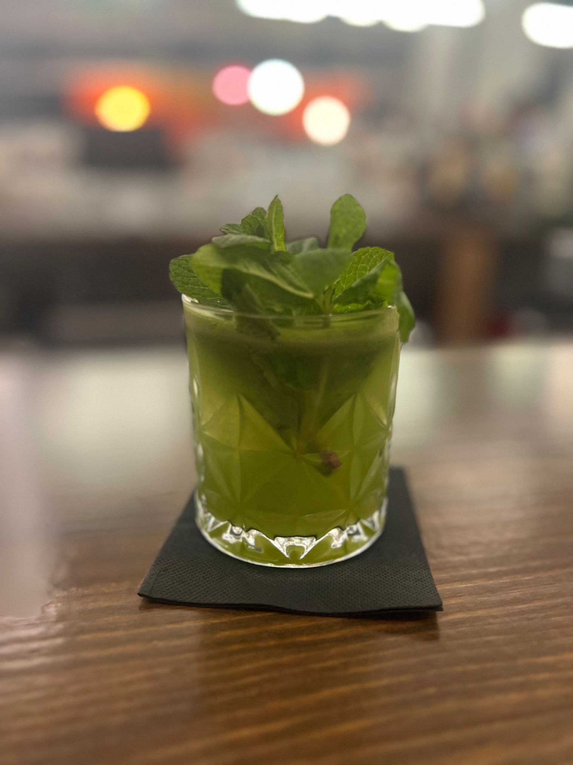 A green drink with mint leaves in a glass on a wooden table.