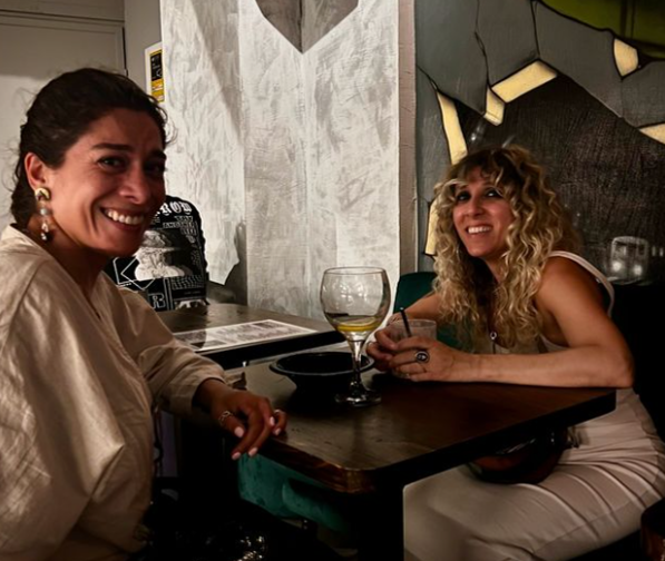 Two women are sitting at a table with glasses of wine