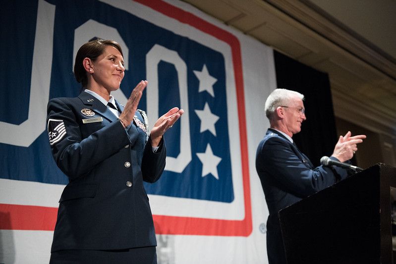 A woman in a military uniform is applauding while standing next to a man at a podium.
