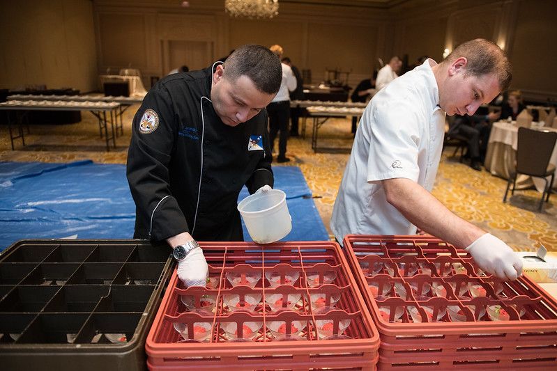 Two men are standing next to each other in a room preparing food.